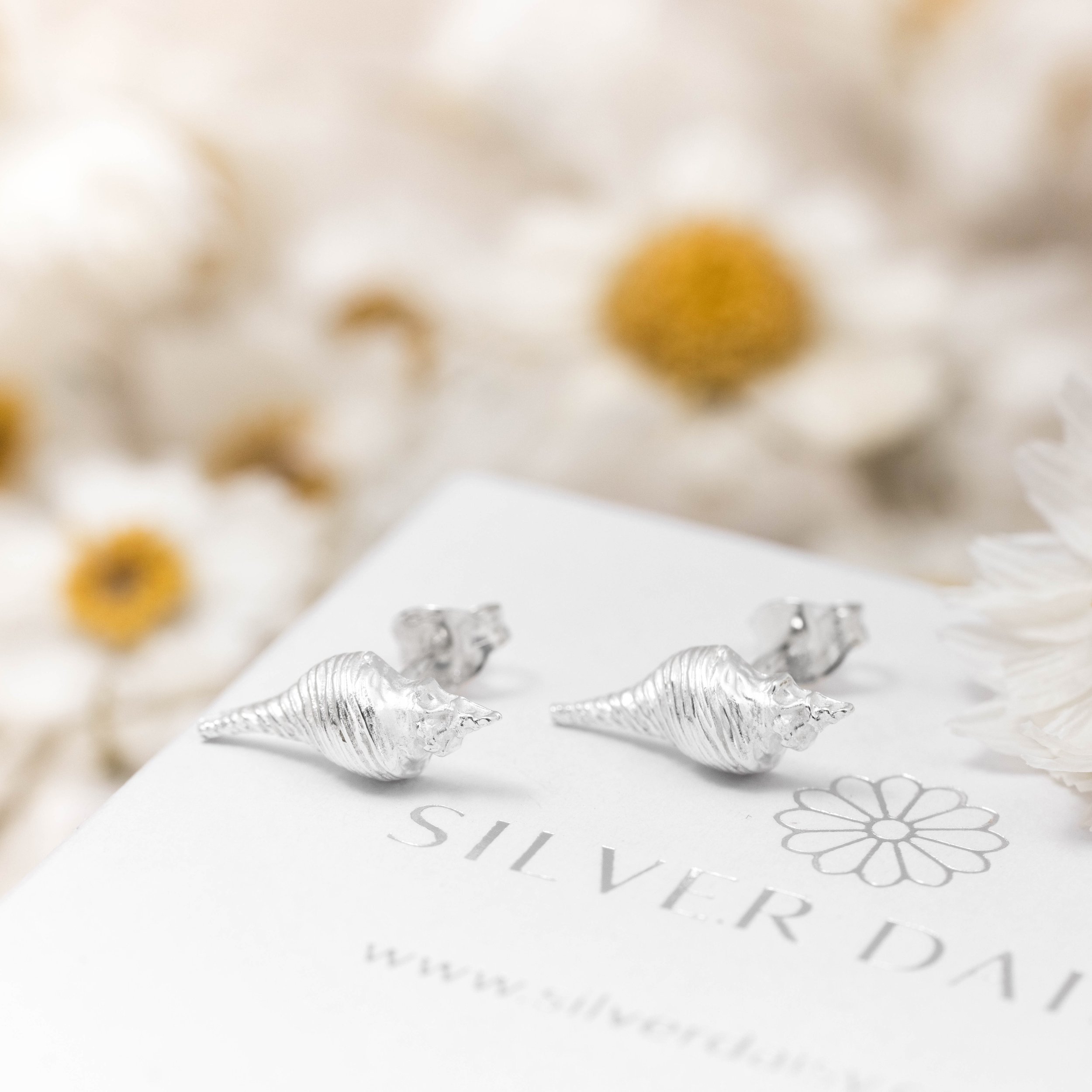 Dainty sterling silver conch shell stud earrings with polished finish, inspired by coastal seashell designs.