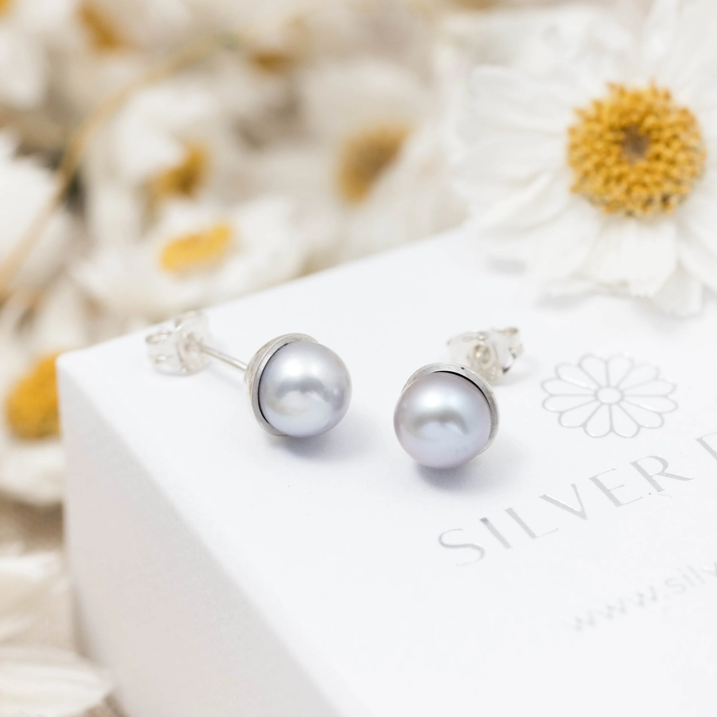 Round grey pearl stud earrings with smooth lustrous finish, set in handcrafted sterling silver cups finished with ear posts and scrolls.