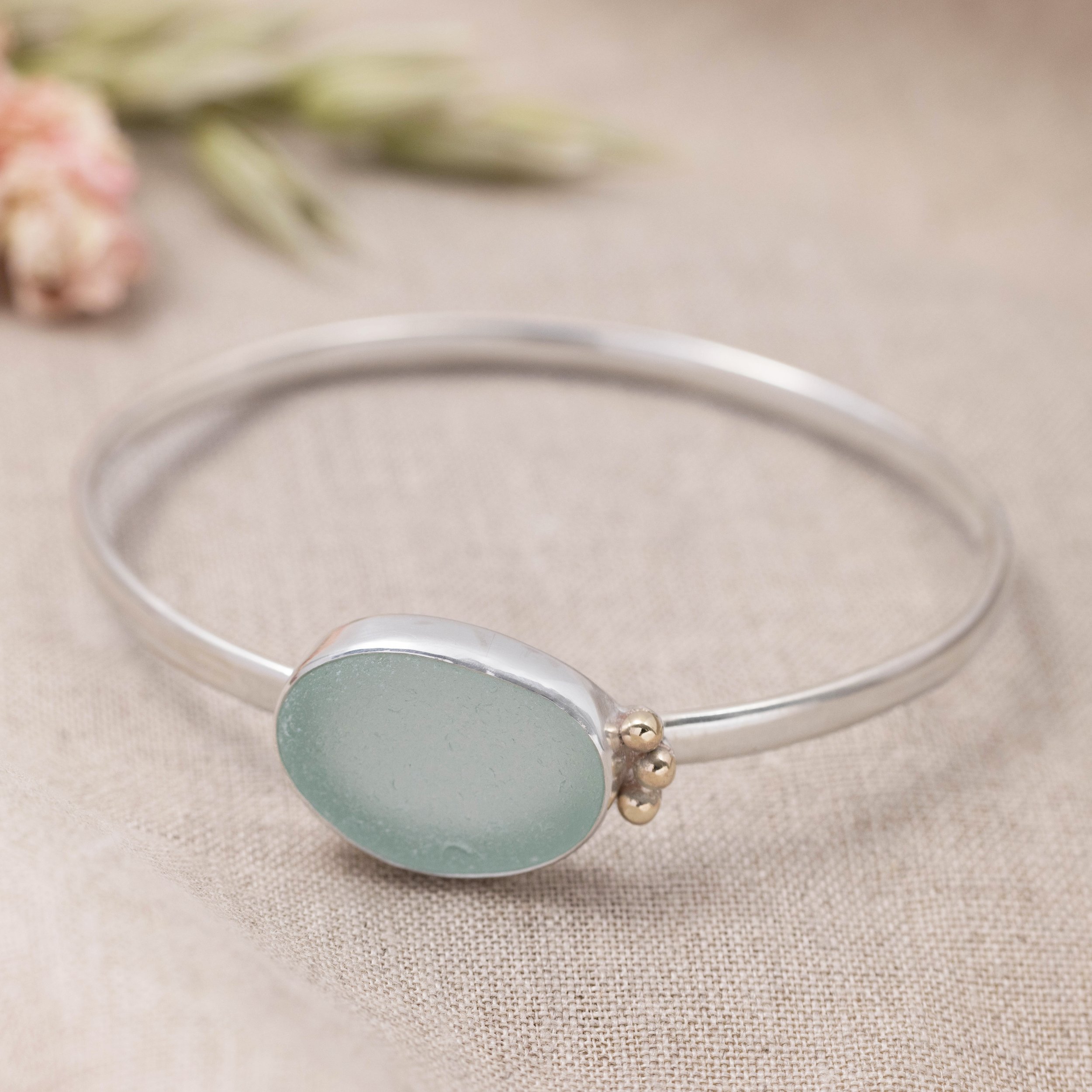 Aquamarine sea glass pebble set with a sterling silver setting and oval band bangle. 9ct gold granulation to highlight. Highly polished finished for this coastal inspired design.