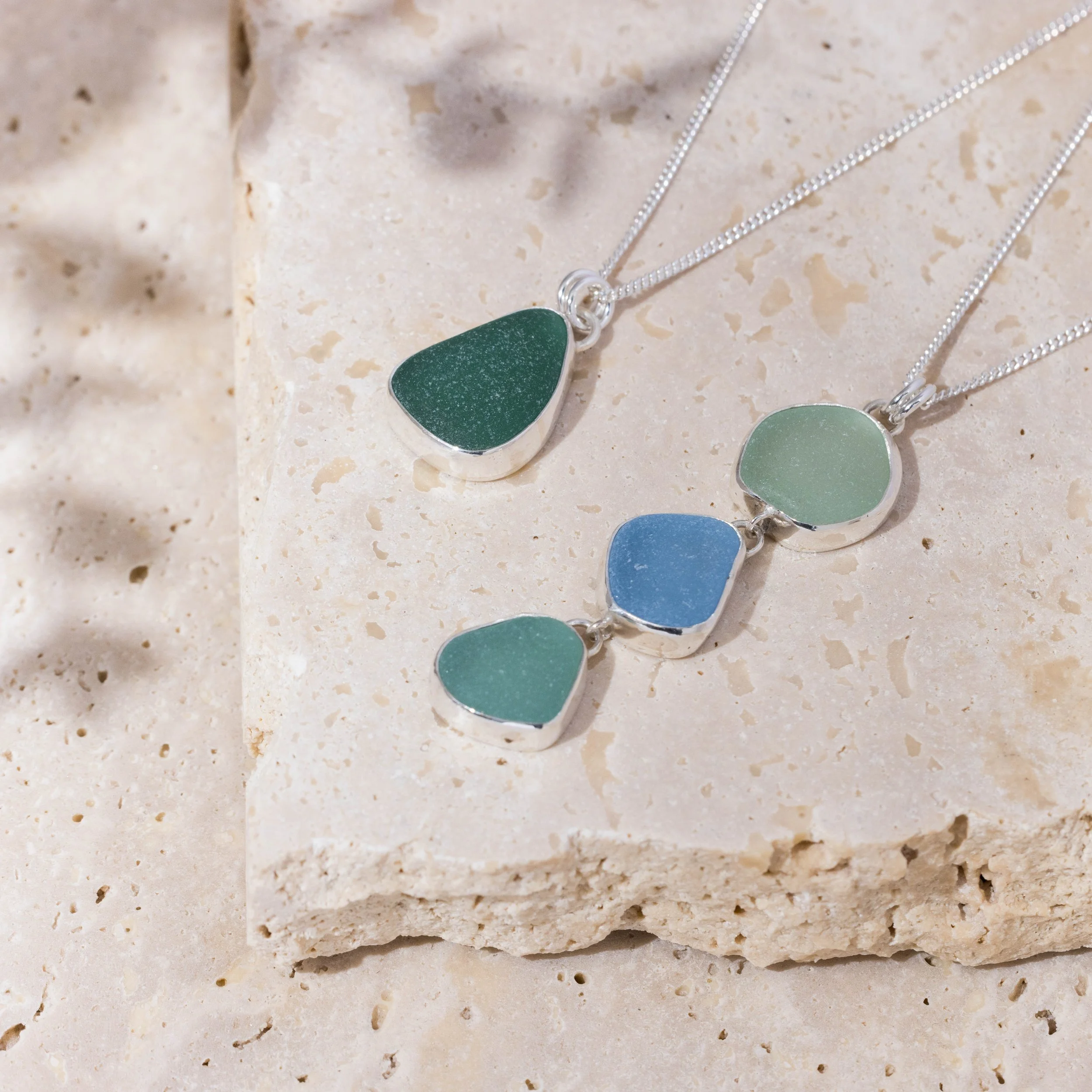 Sterling silver pendant necklace with cascading multi-coloured sea glass drops in green and blue tones, inspired by coastal style.