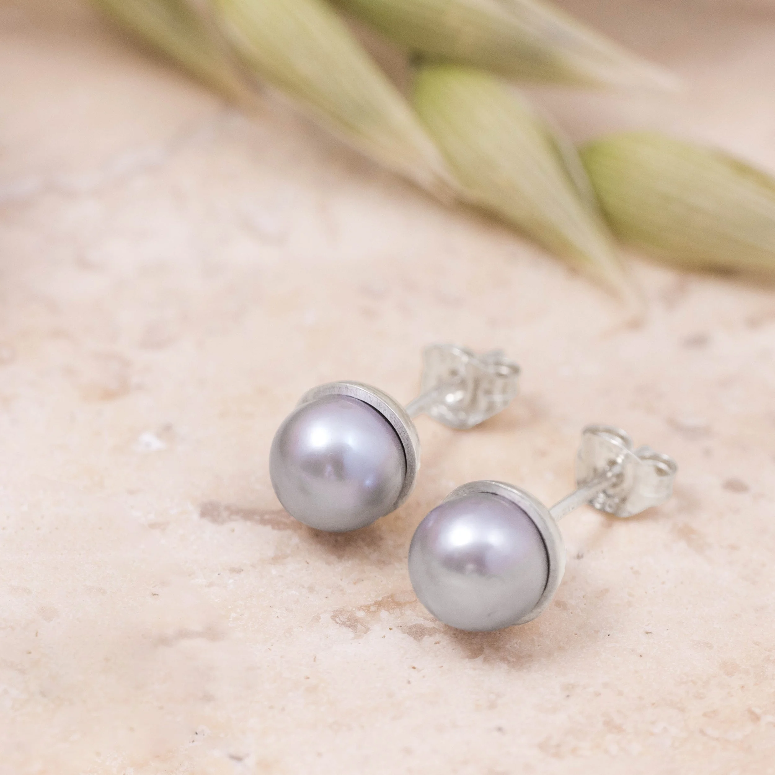 Round grey pearl stud earrings with smooth lustrous finish, set in handcrafted sterling silver cups finished with ear posts and scrolls.