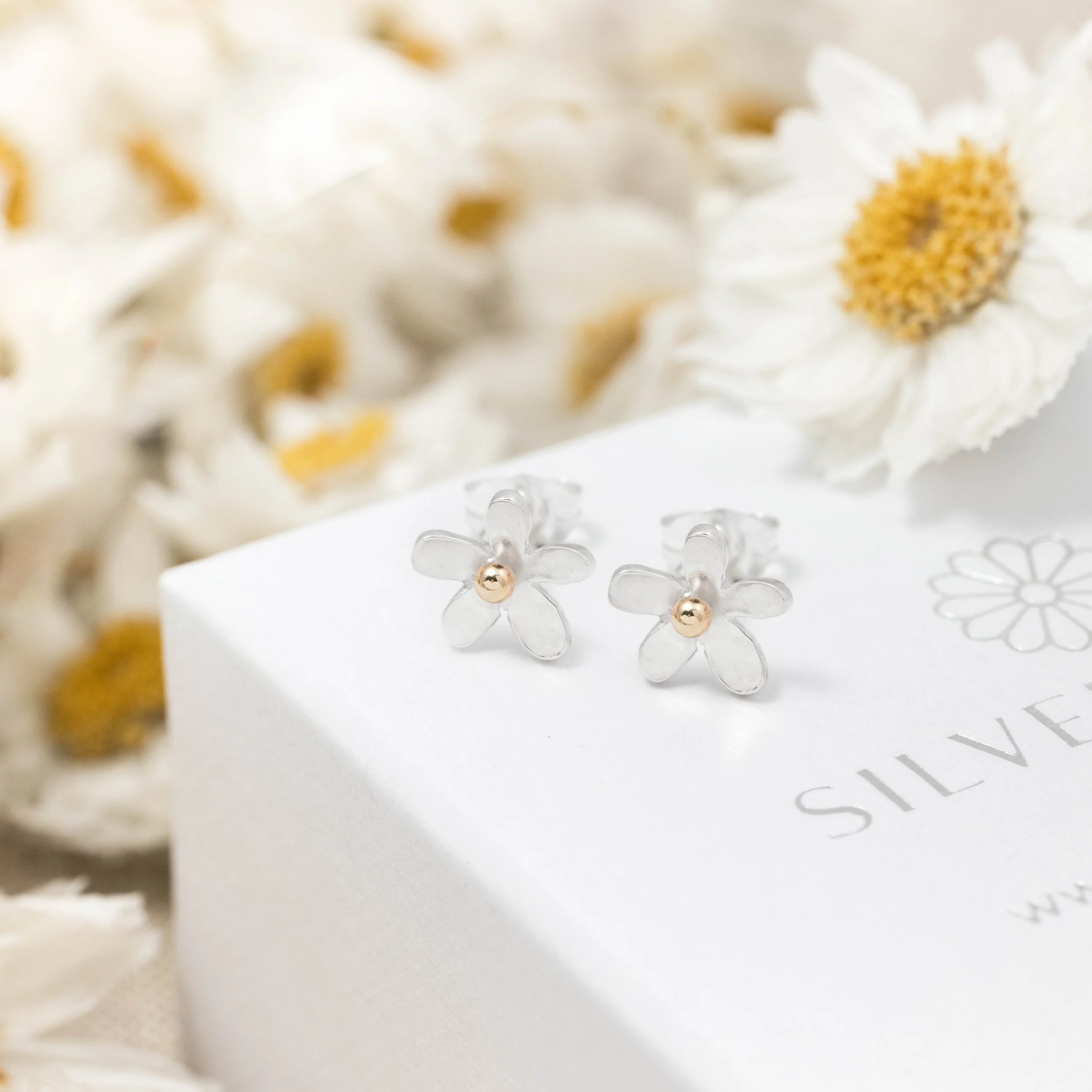 Small sterling silver daisy stud earrings with polished petals and 9ct gold stamen centres.