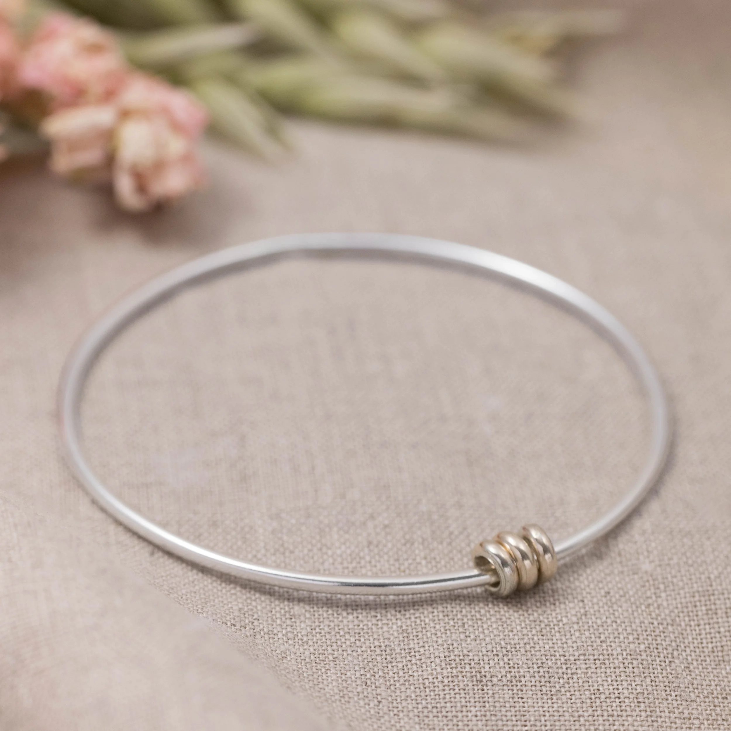 Sterling silver bangle with polished 9ct gold satellite rings which move freely around the band. An elegant fidget bracelet.