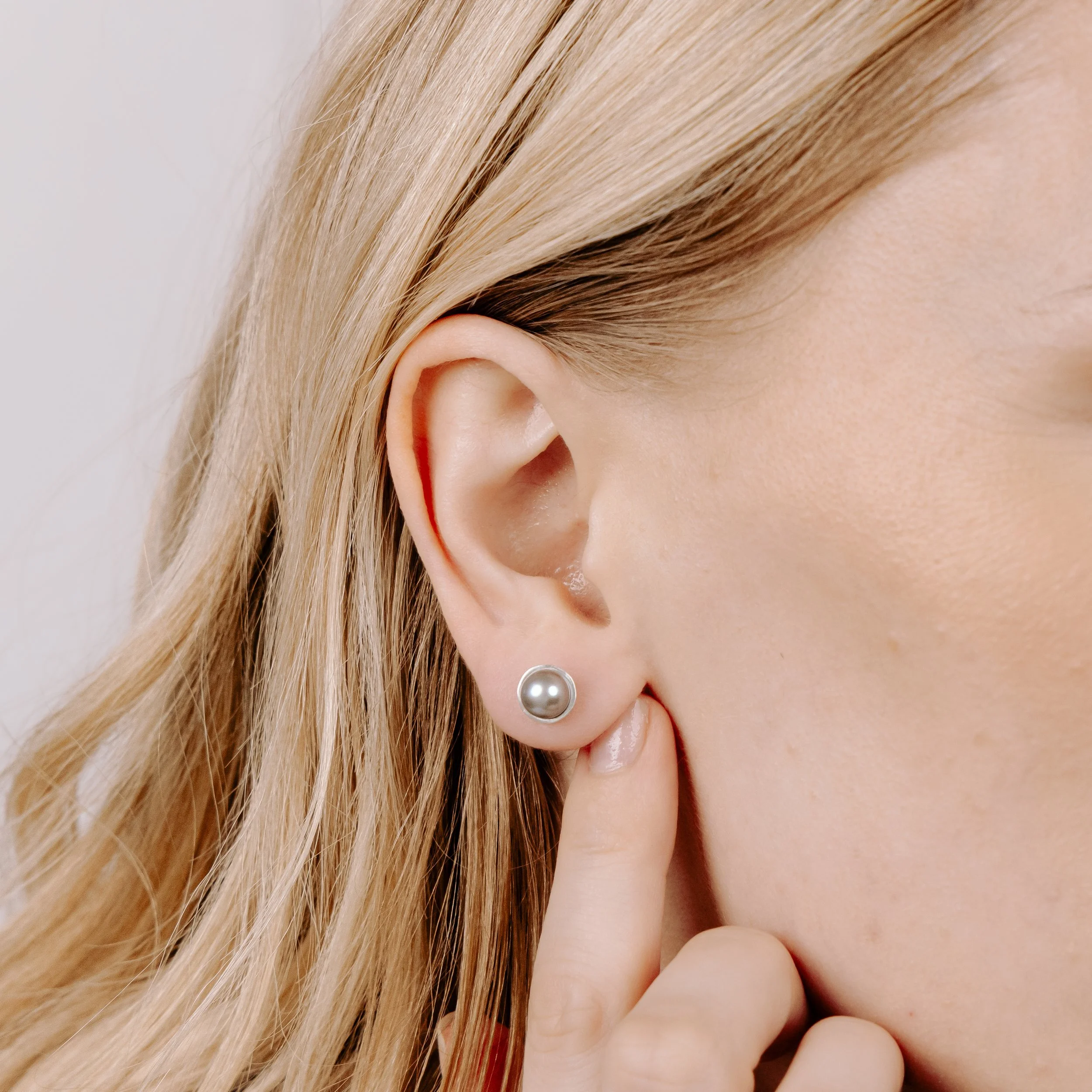 Round grey pearl stud earrings with smooth lustrous finish, set in handcrafted sterling silver cups finished with ear posts and scrolls.