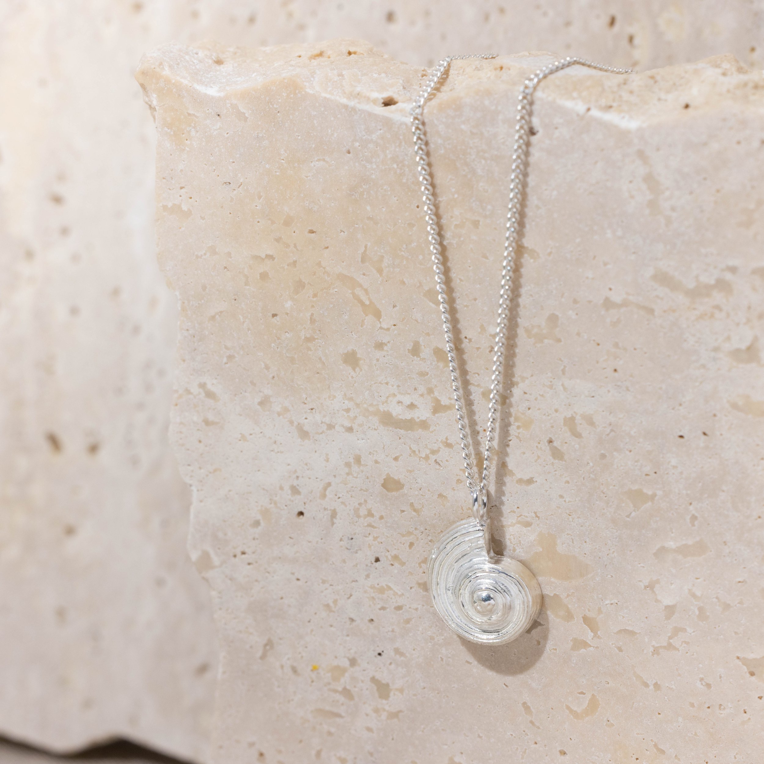 Sterling silver pendant necklace with a detailed fossil ammonite design on a fine chain, inspired by coastal and seaside jewellery.