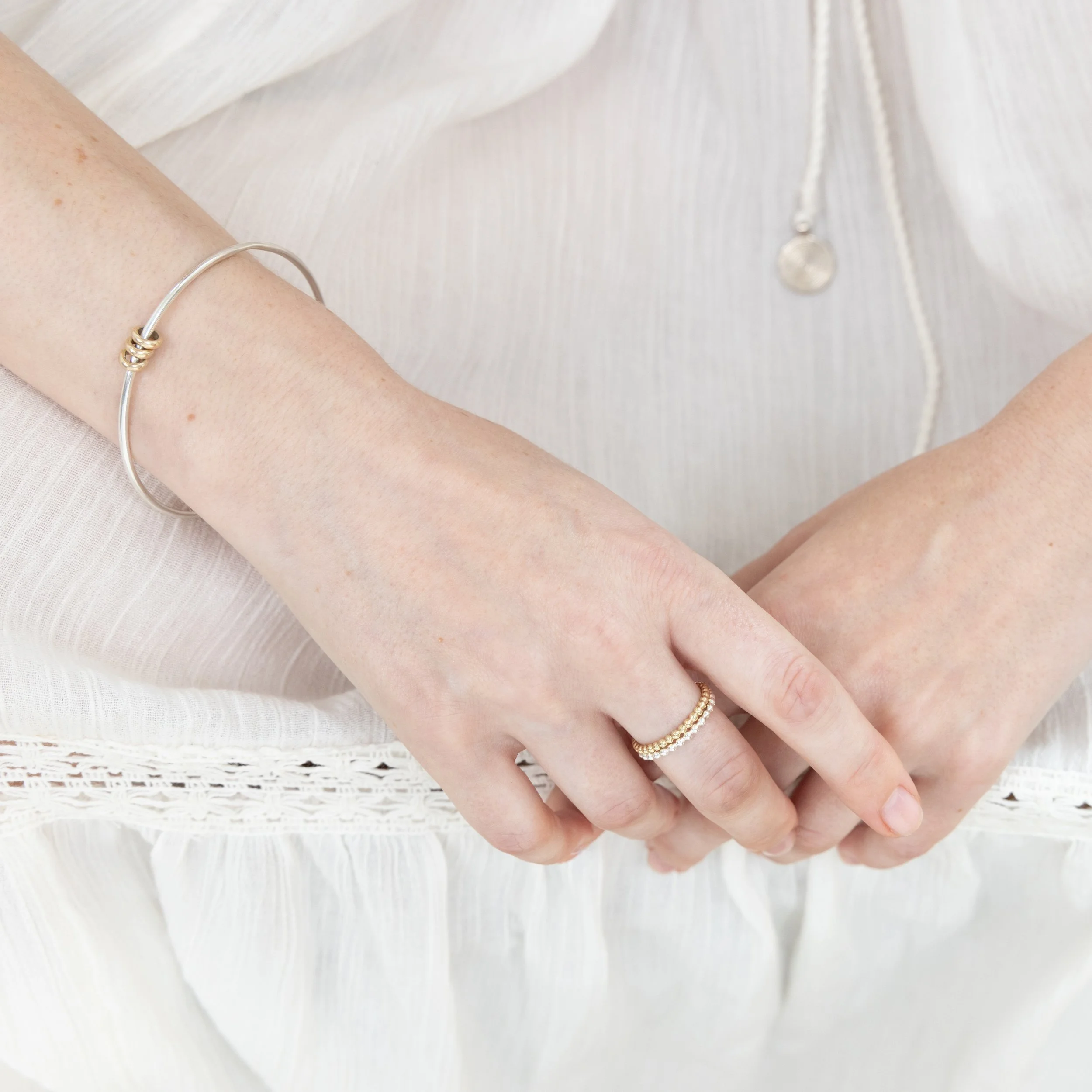 Sterling silver bangle with polished 9ct gold satellite rings which move freely around the band. An elegant fidget bracelet.