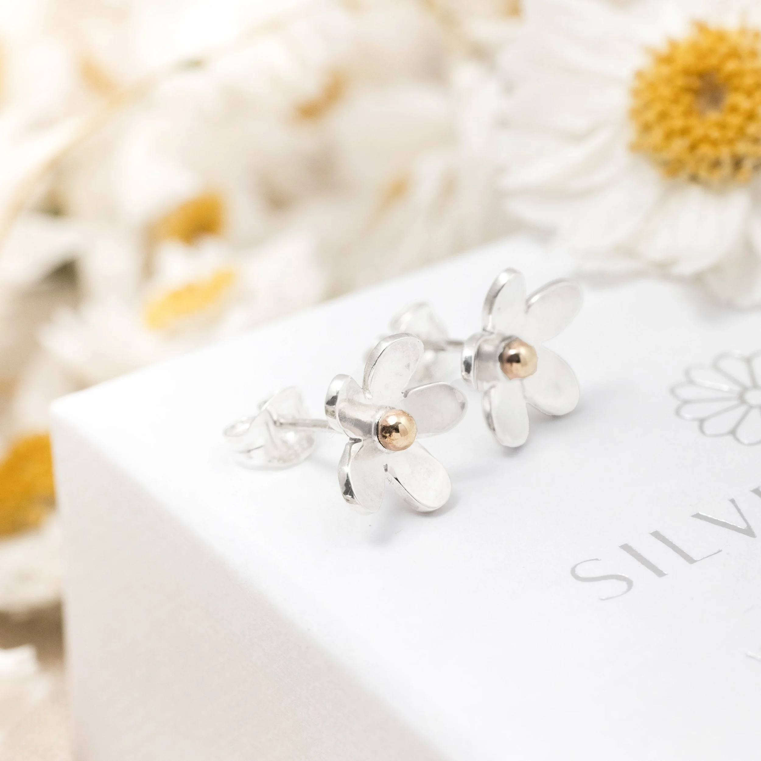 Handmade silver daisy stud earrings with polished petals and 9ct gold stamen centres.