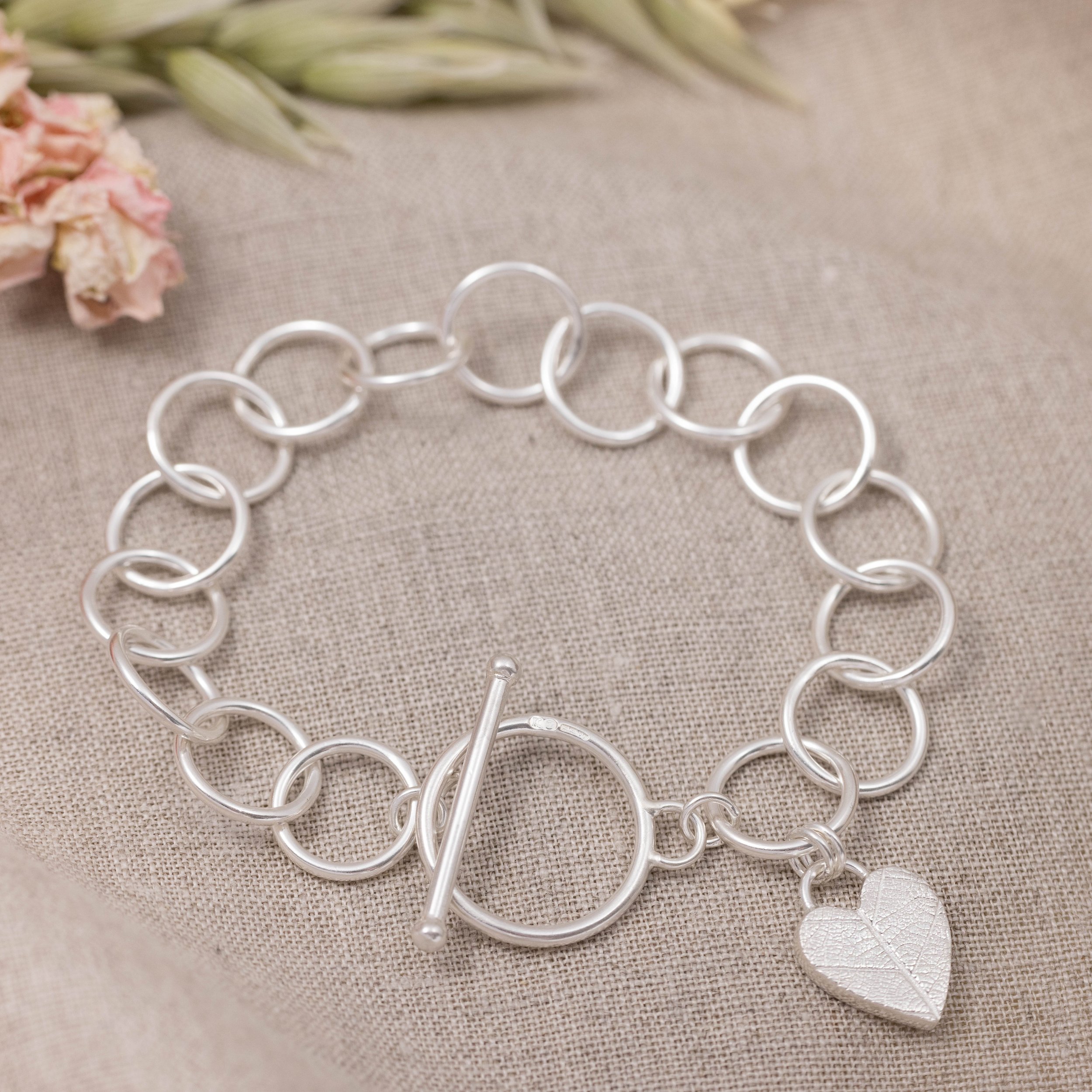 Sterling silver bracelet with a textured heart charm featuring a delicate leaf pattern, finished with a toggle clasp.
