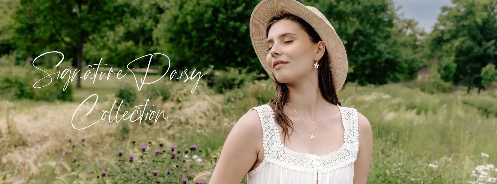 Signature Daisy Jewellery Collection page header features a summary scene with brown haired model in a lace dress and sunhat wearing silver daisy earrings and necklace. The background is a summer meadow in bloom with wild flowers.