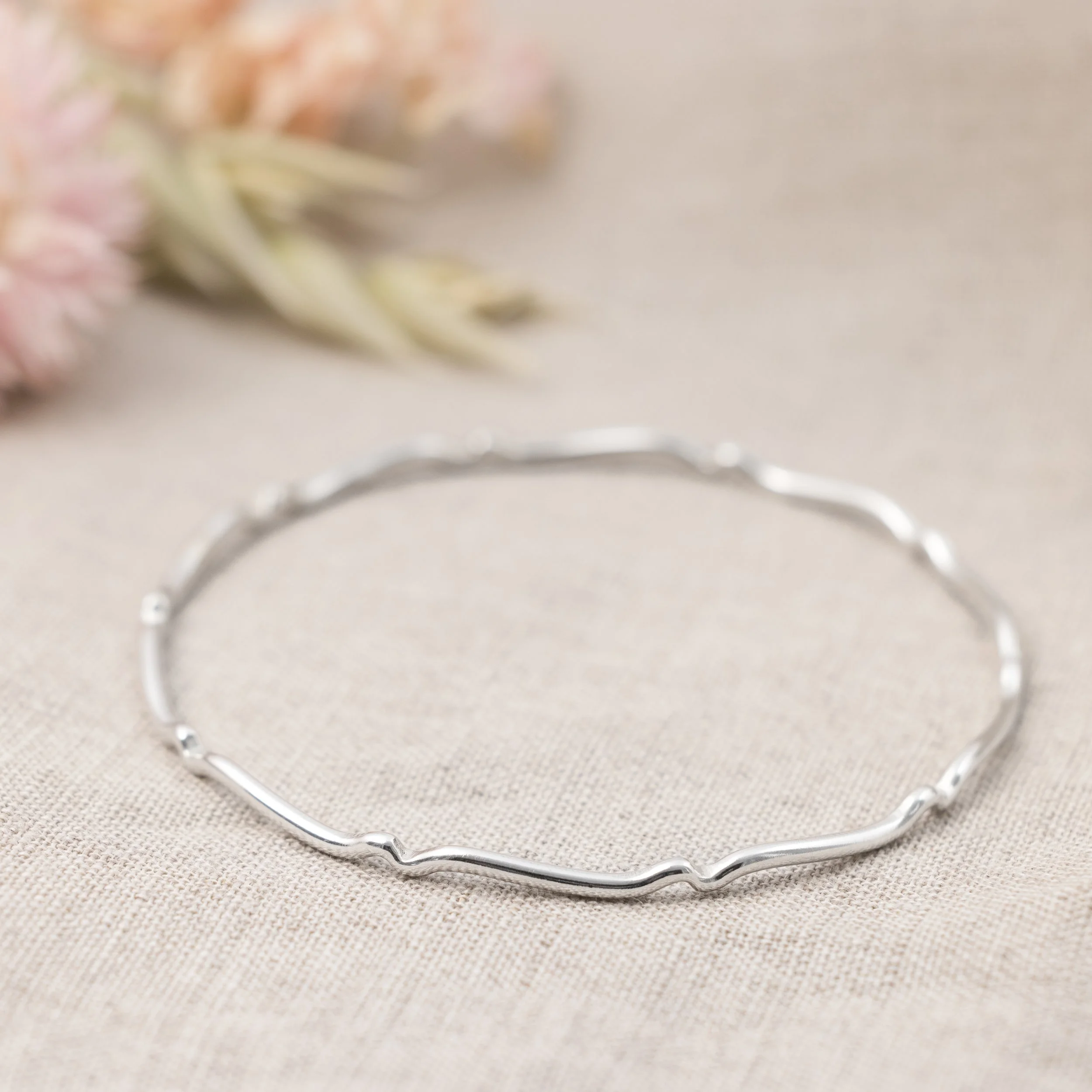 Sterling silver scalloped bangle with polished finish, featuring a wavy edge design for elegant stacking or standalone wear.