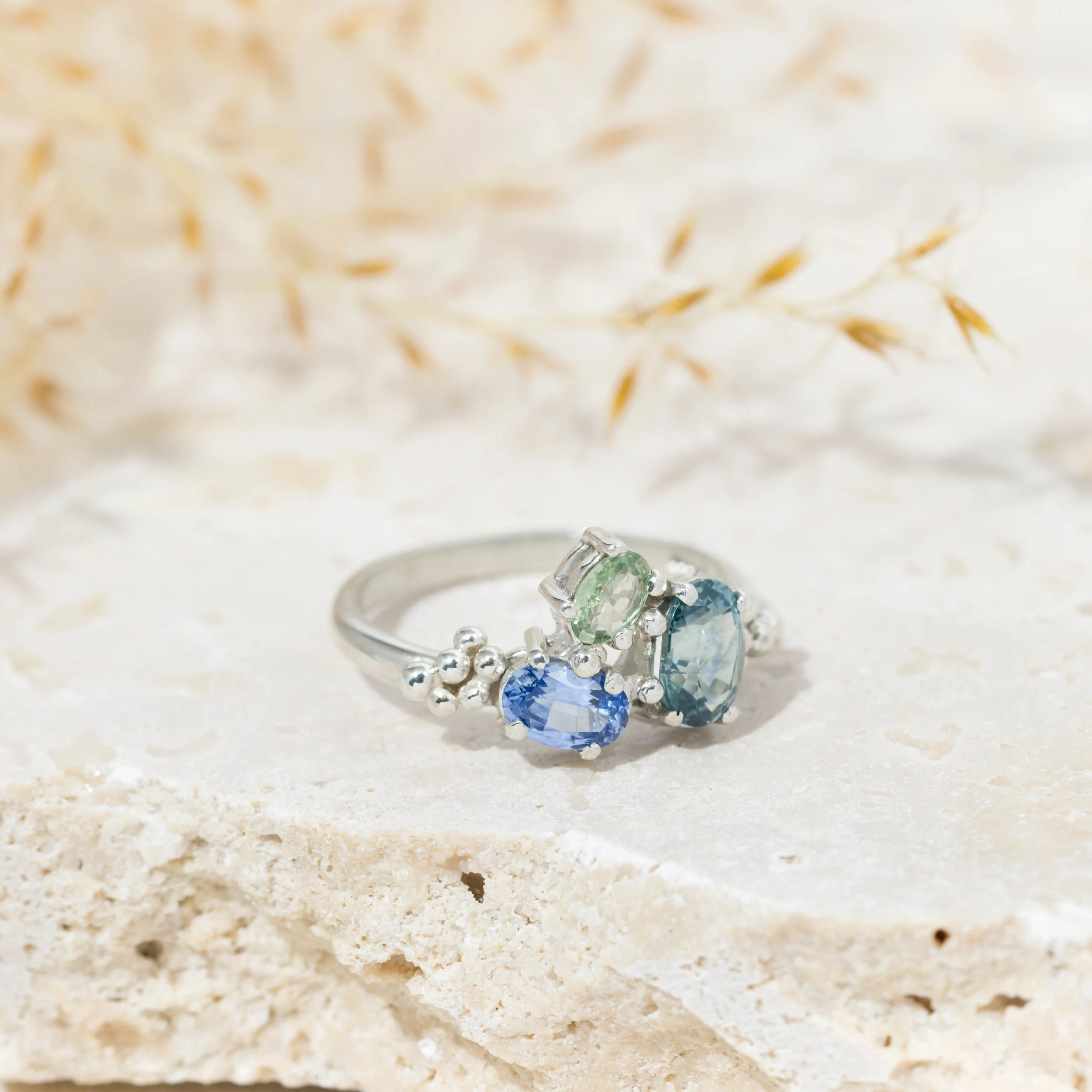 White gold ring with a cluster of oval blue and green sapphires in a seascape-inspired design.