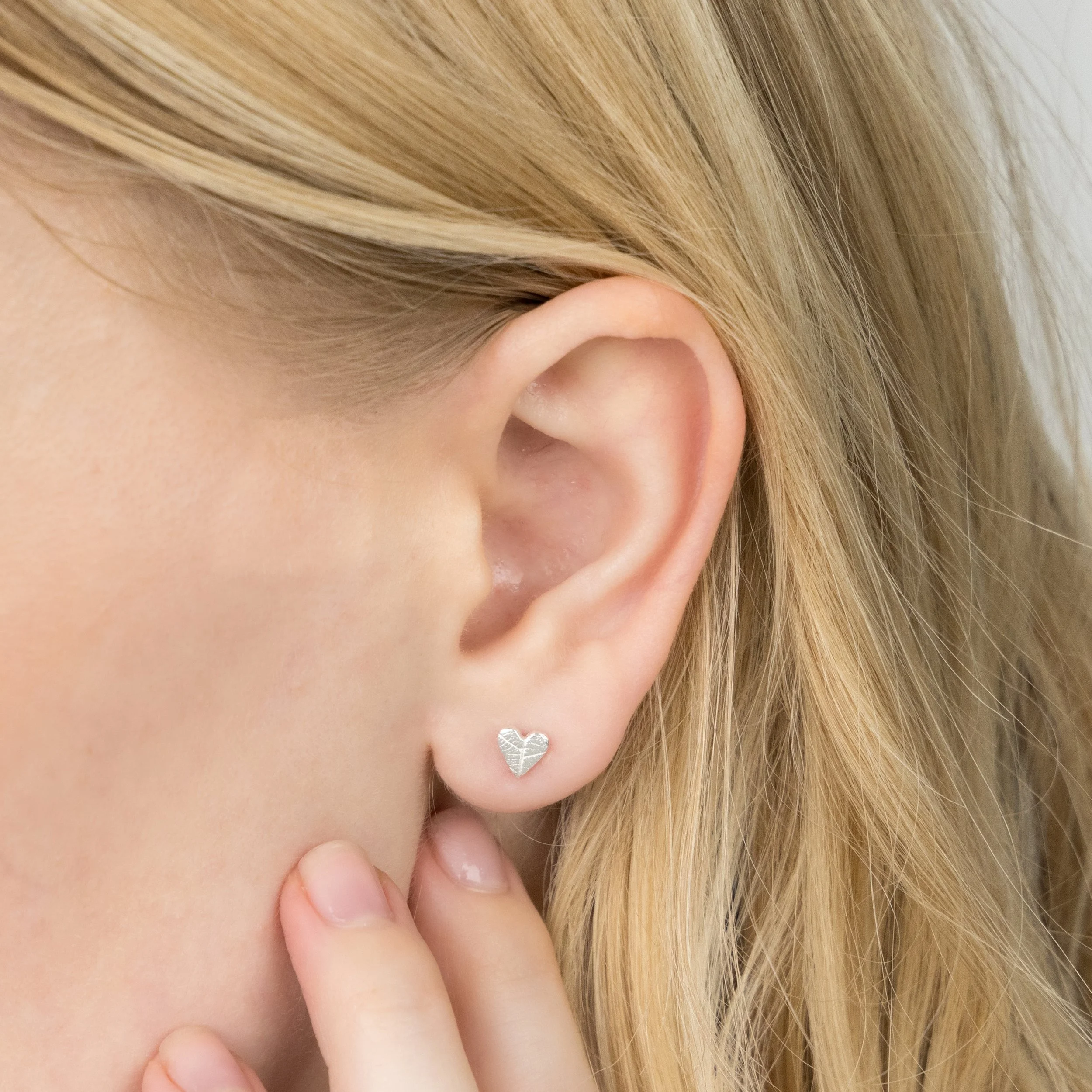 Mini sterling silver heart stud earrings with delicate leaf vein texture, polished finish, and butterfly backs.