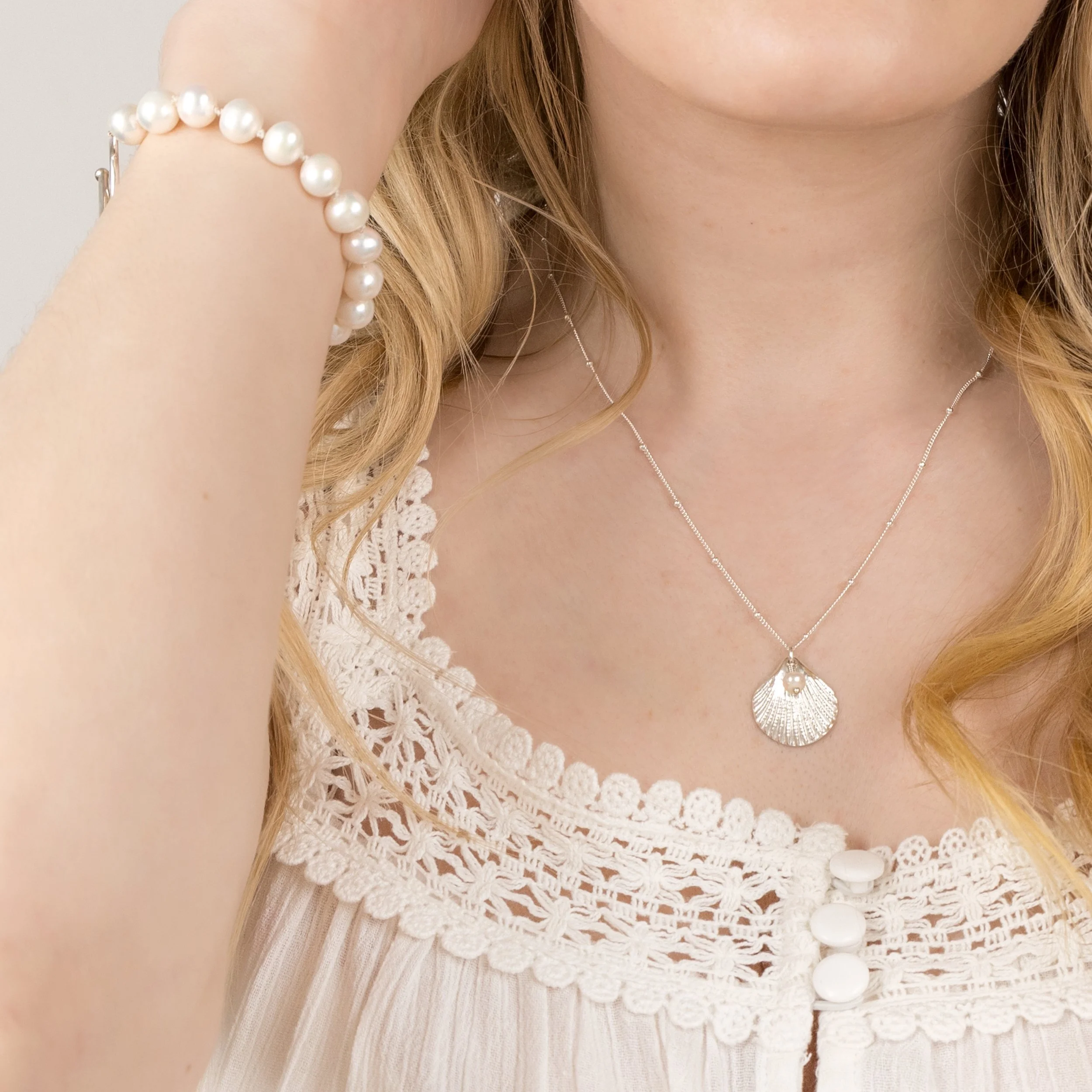 Silver scallop shell pendant necklace with a single white pearl on a delicate chain, inspired by coastal jewellery design.