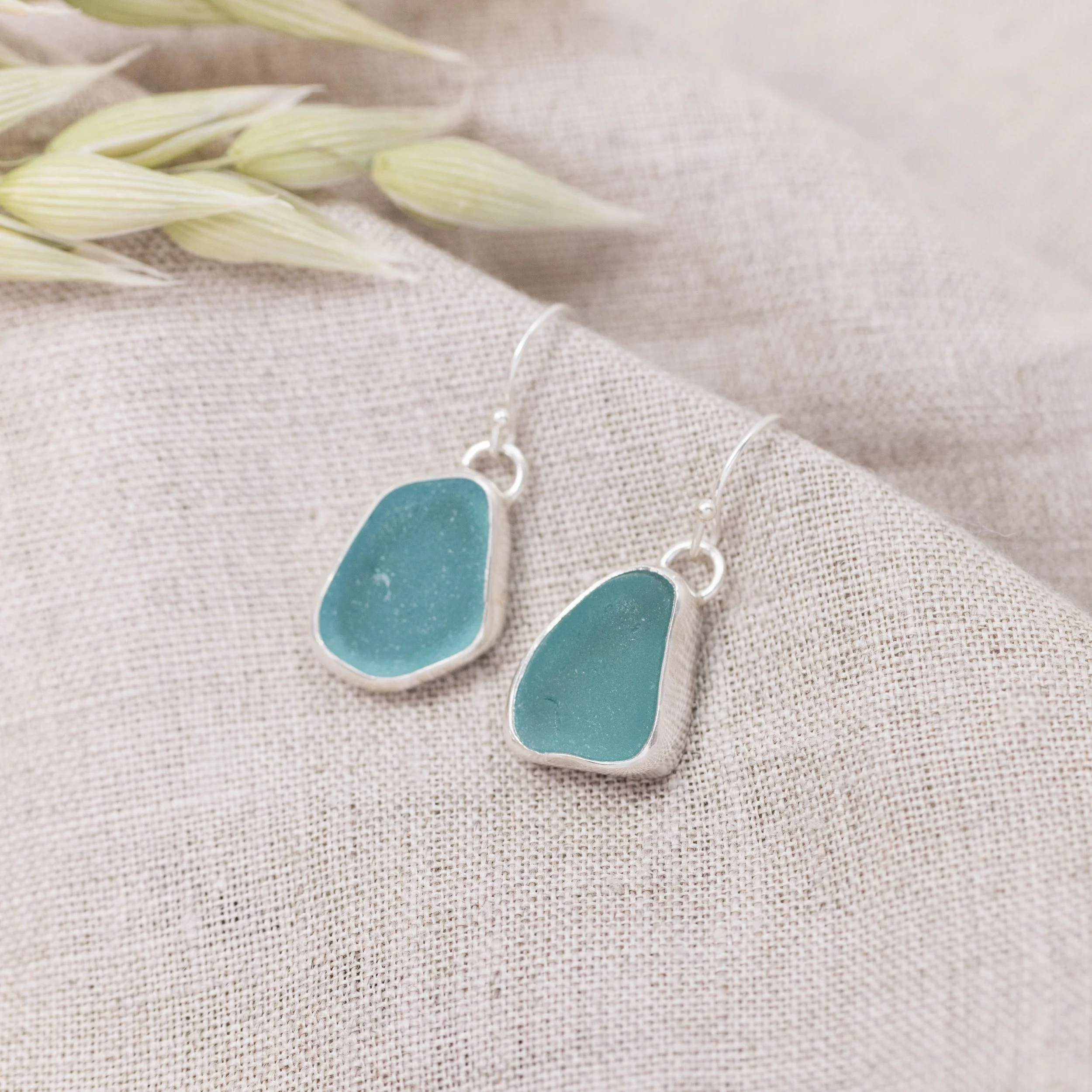 Sterling silver drop earrings with smooth teardrop teal sea glass, hanging from simple hooks in a coastal-inspired design.