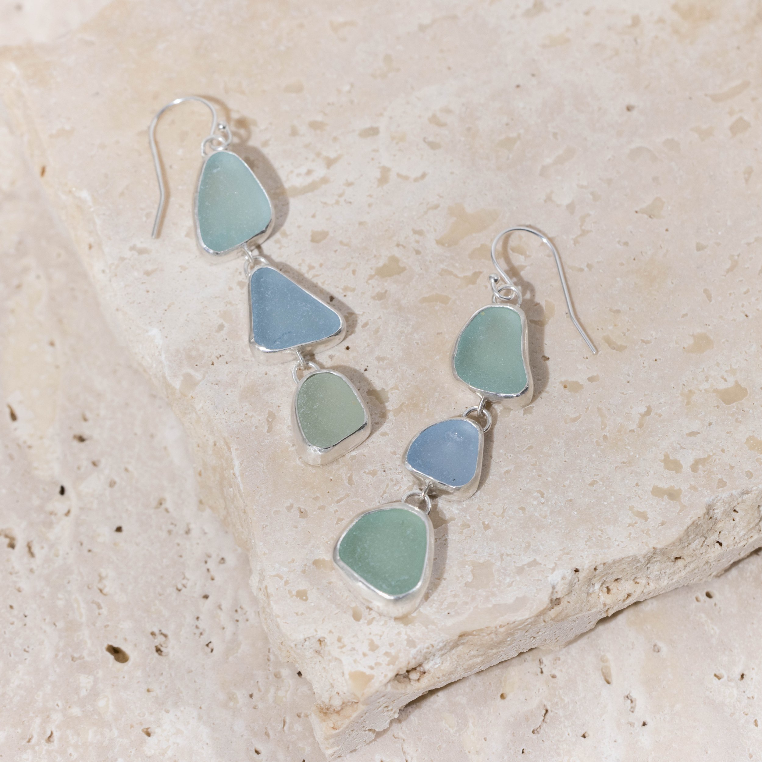 Sterling silver drop earrings with cascading multi-coloured sea glass pieces in green and blue tones on delicate ear wires. Coastal inspired jewellery design.