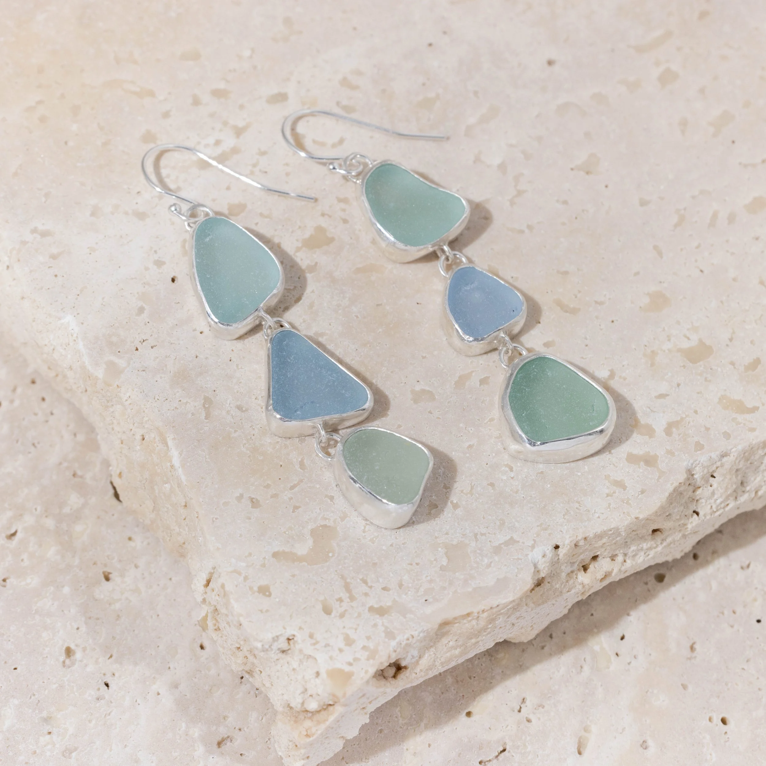 Sterling silver drop earrings with cascading multi-coloured sea glass pieces in green and blue tones on delicate ear wires. Coastal inspired jewellery design.