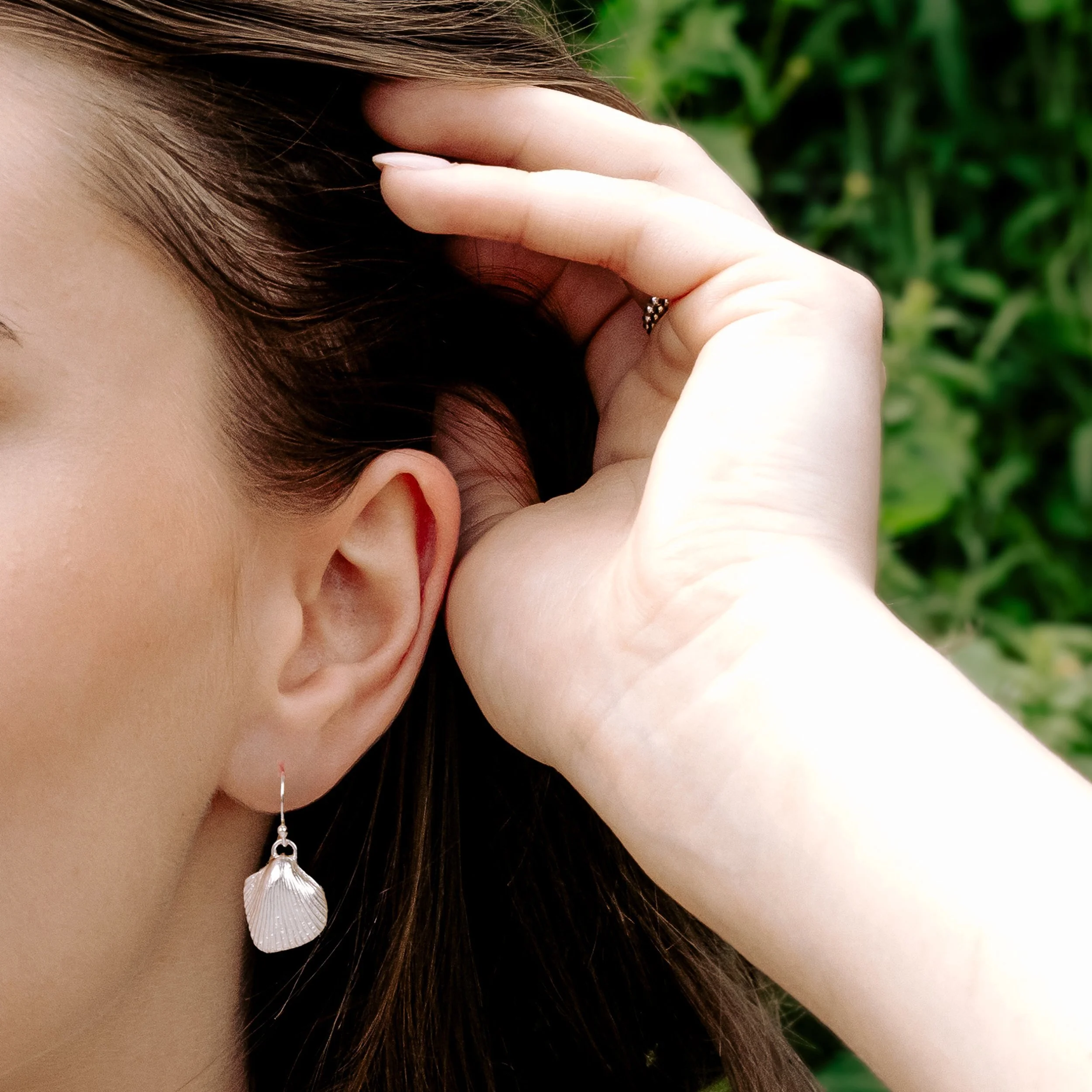 Sterling silver cockle shell drop earrings with detailed textured shells and polished finish, hanging from simple hook wires.