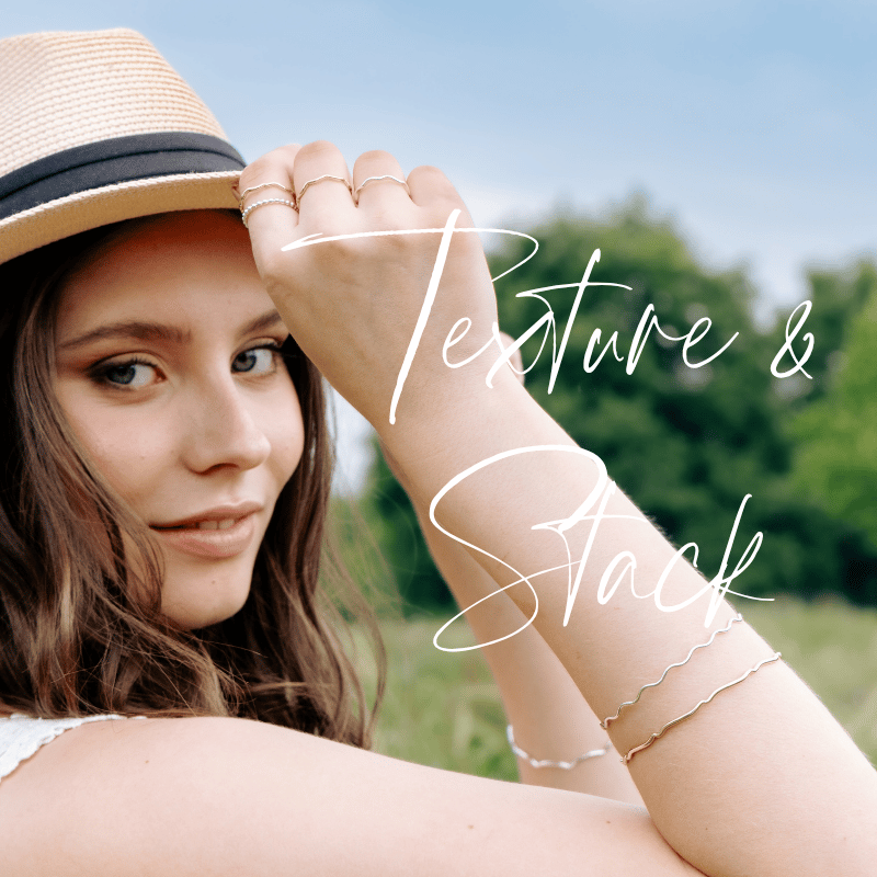 A woman outdoors wearing a hat, and stacking rings and bangles in silver and gold looking at the camera with a slight smile, and text overlay that reads 'Texture & Stack' in elegant cursive.
