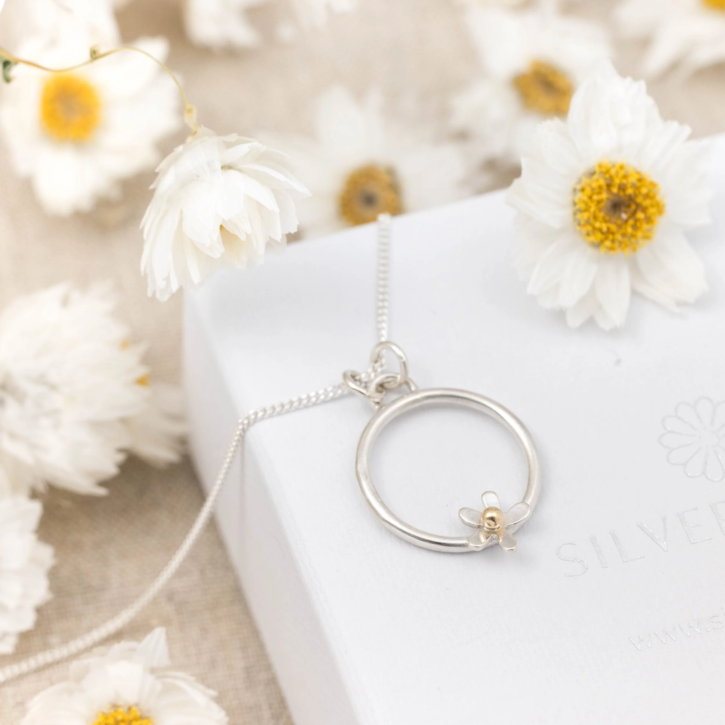 Sterling silver hoop pendant necklace with an open daisy flower design featuring a 9ct gold stamen on a fine chain, polished finish, minimalist floral jewellery.