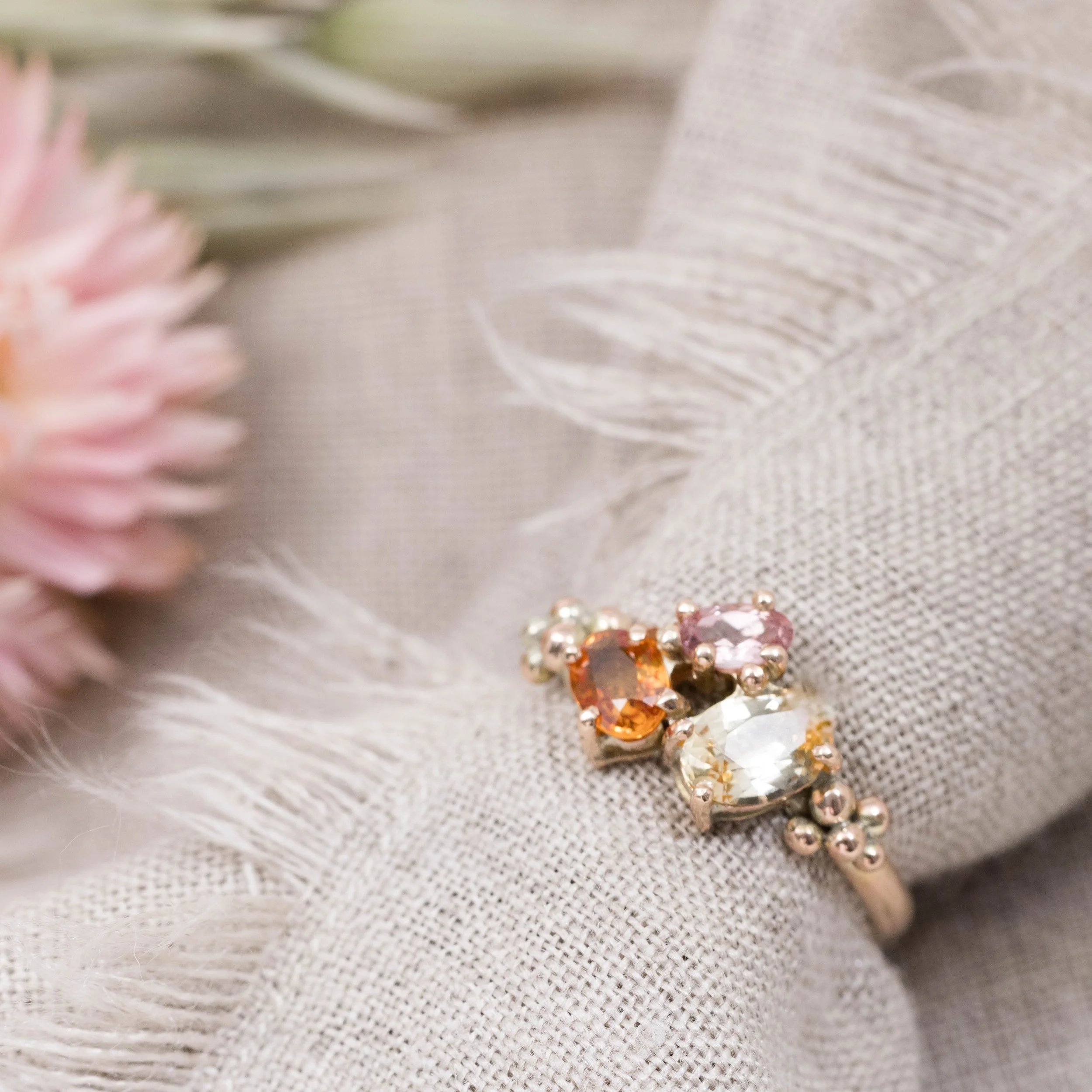 Rose gold ring with an oval orange sapphire centre surrounded by a cluster of round pink and yellow sapphires.