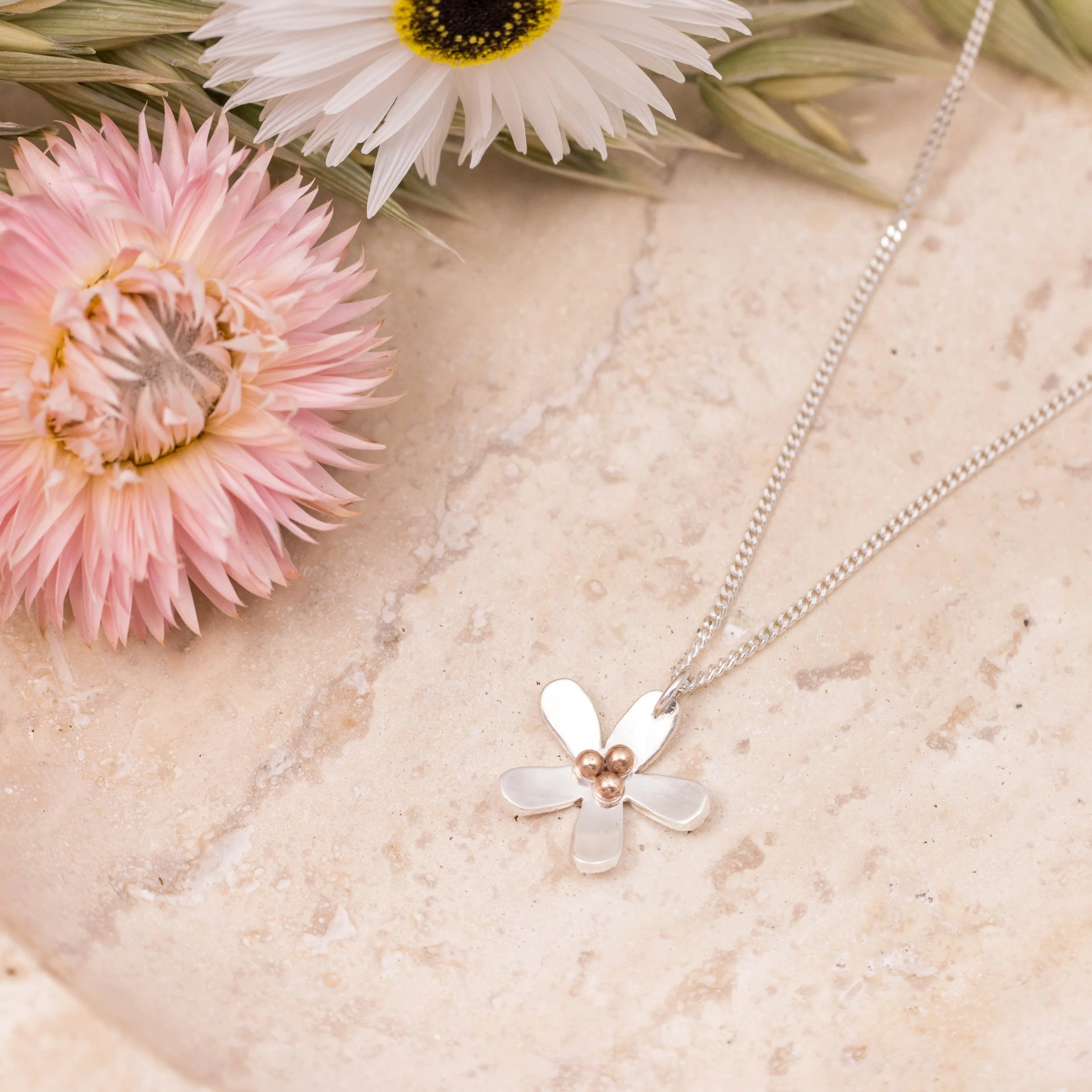 Sterling silver daisy pendant necklace with polished petals and a 9ct gold stamen on a delicate silver chain.