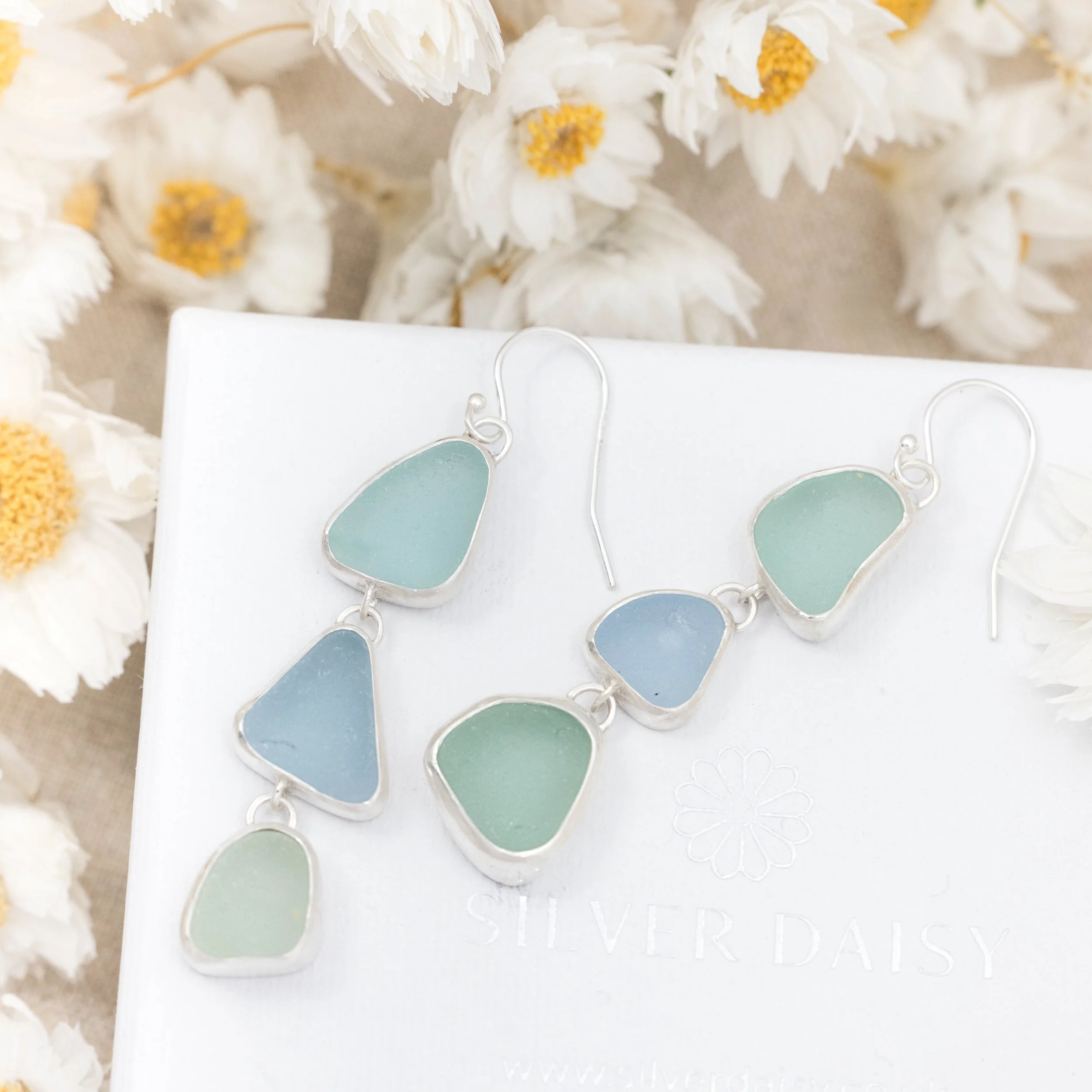 Sterling silver drop earrings with cascading multi-coloured sea glass pieces in green and blue tones on delicate ear wires. Coastal inspired jewellery design.