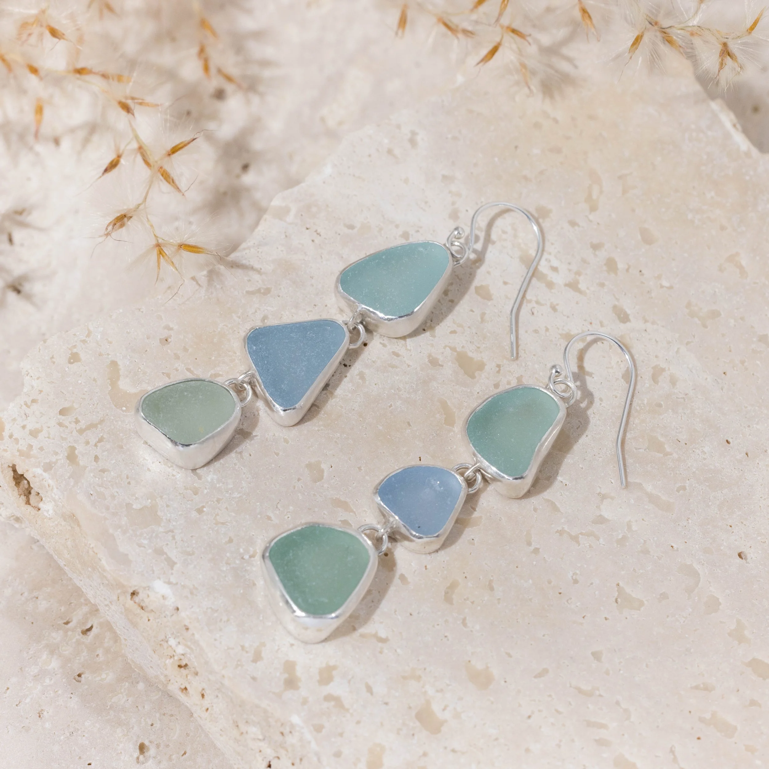 Sterling silver drop earrings with cascading multi-coloured sea glass pieces in green and blue tones on delicate ear wires. Coastal inspired jewellery design.