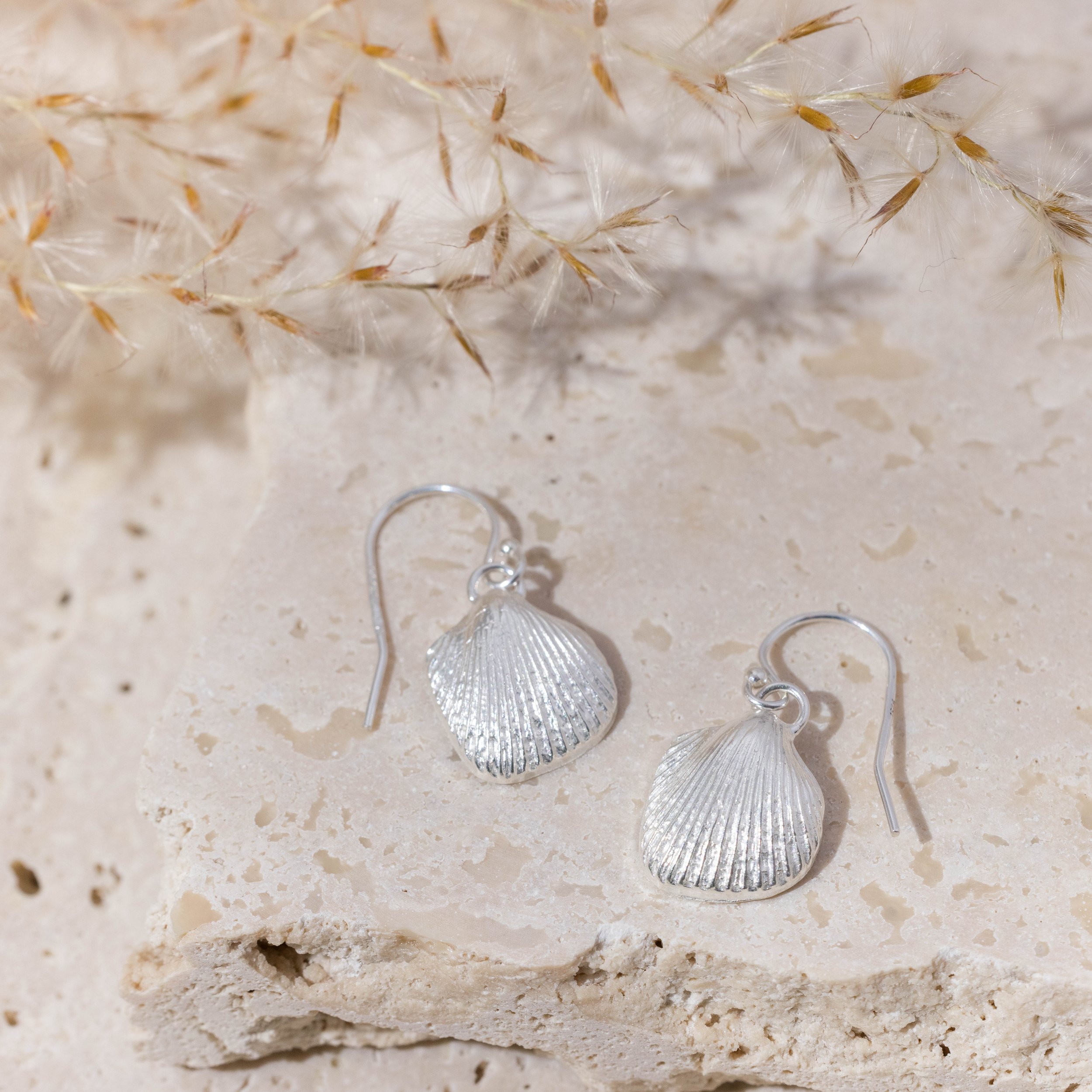 Sterling silver cockle shell drop earrings with detailed textured shells and polished finish, hanging from simple hook wires.