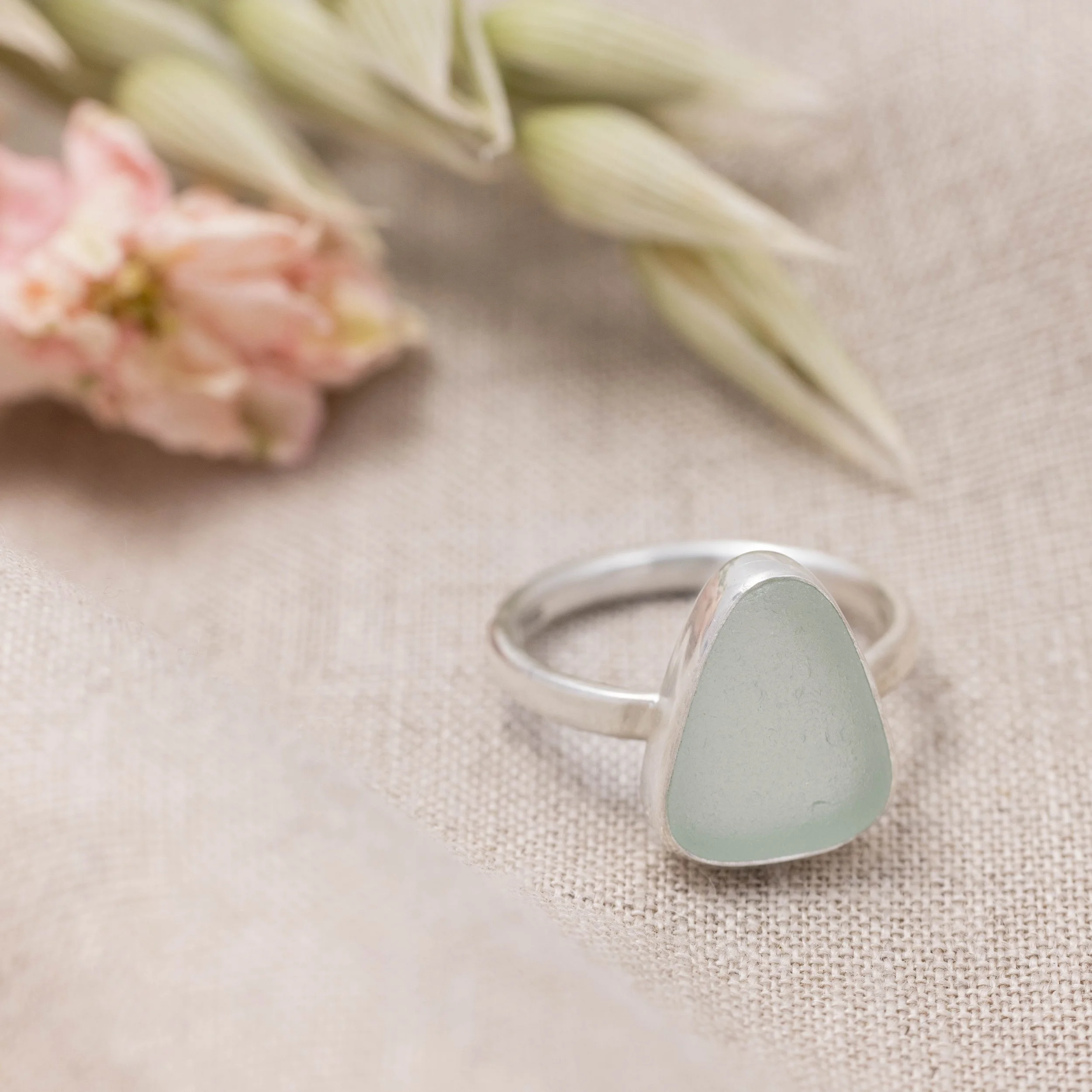 Sterling silver ring with a smooth aquamarine sea glass gemstone in a polished bezel setting on a slim oval band. Coastal beach inspired jewellery.