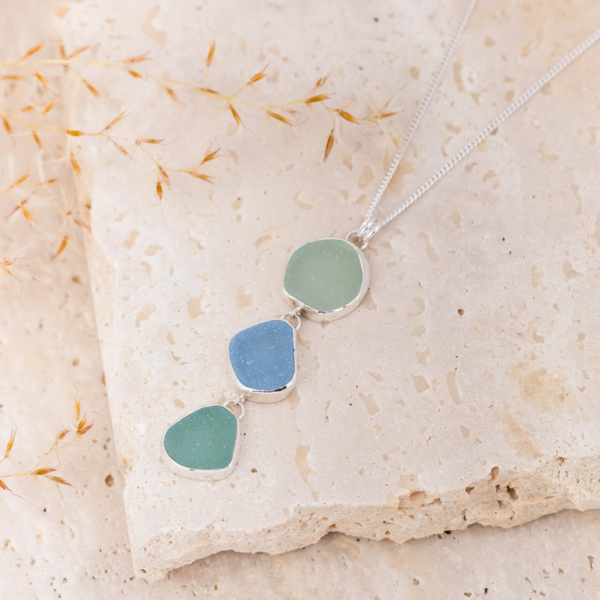 Sterling silver pendant necklace with cascading multi-coloured sea glass drops in green and blue tones, inspired by coastal style.