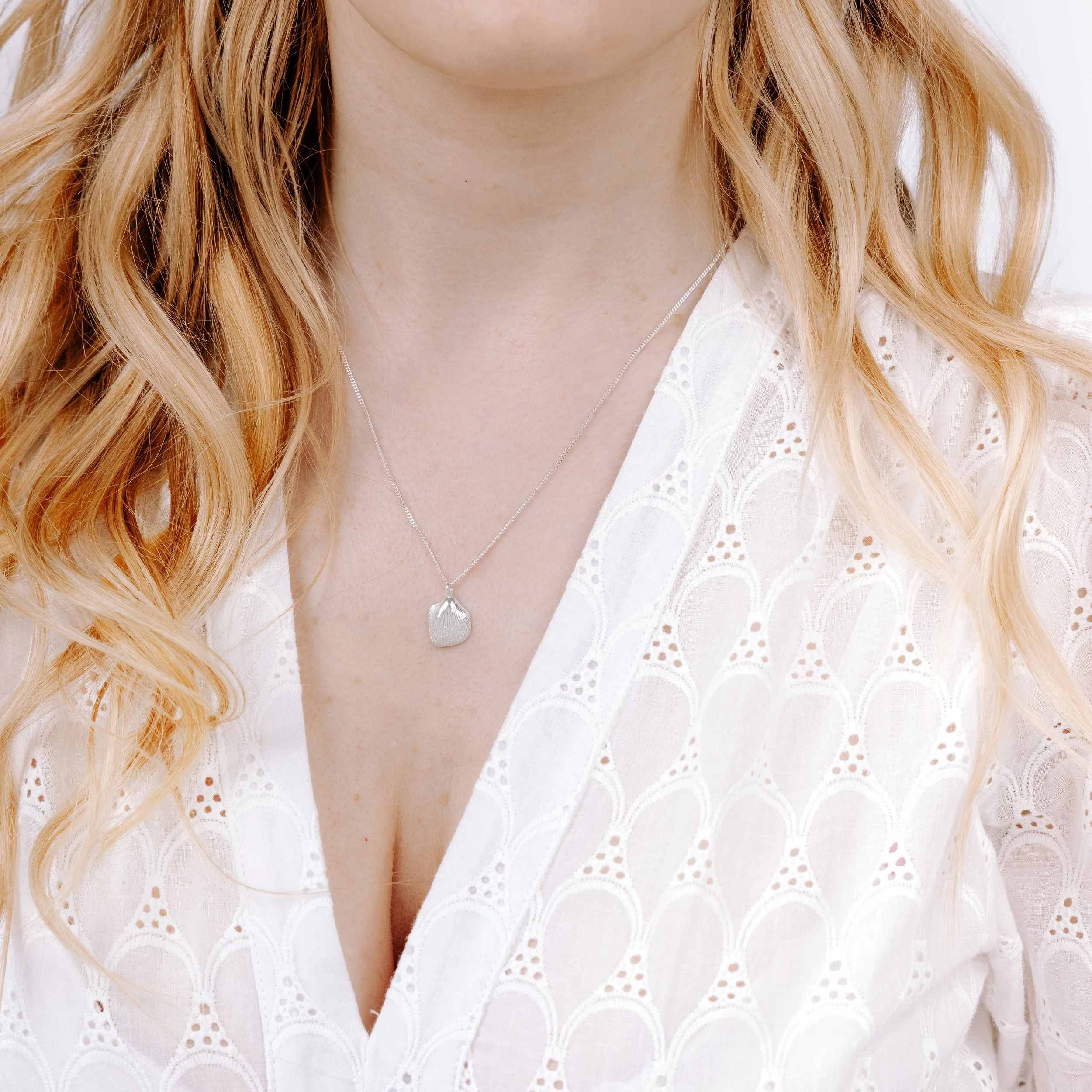 Sterling silver cockle shell pendant necklace with fine detailing on a delicate silver chain, inspired by coastal beachcombing.