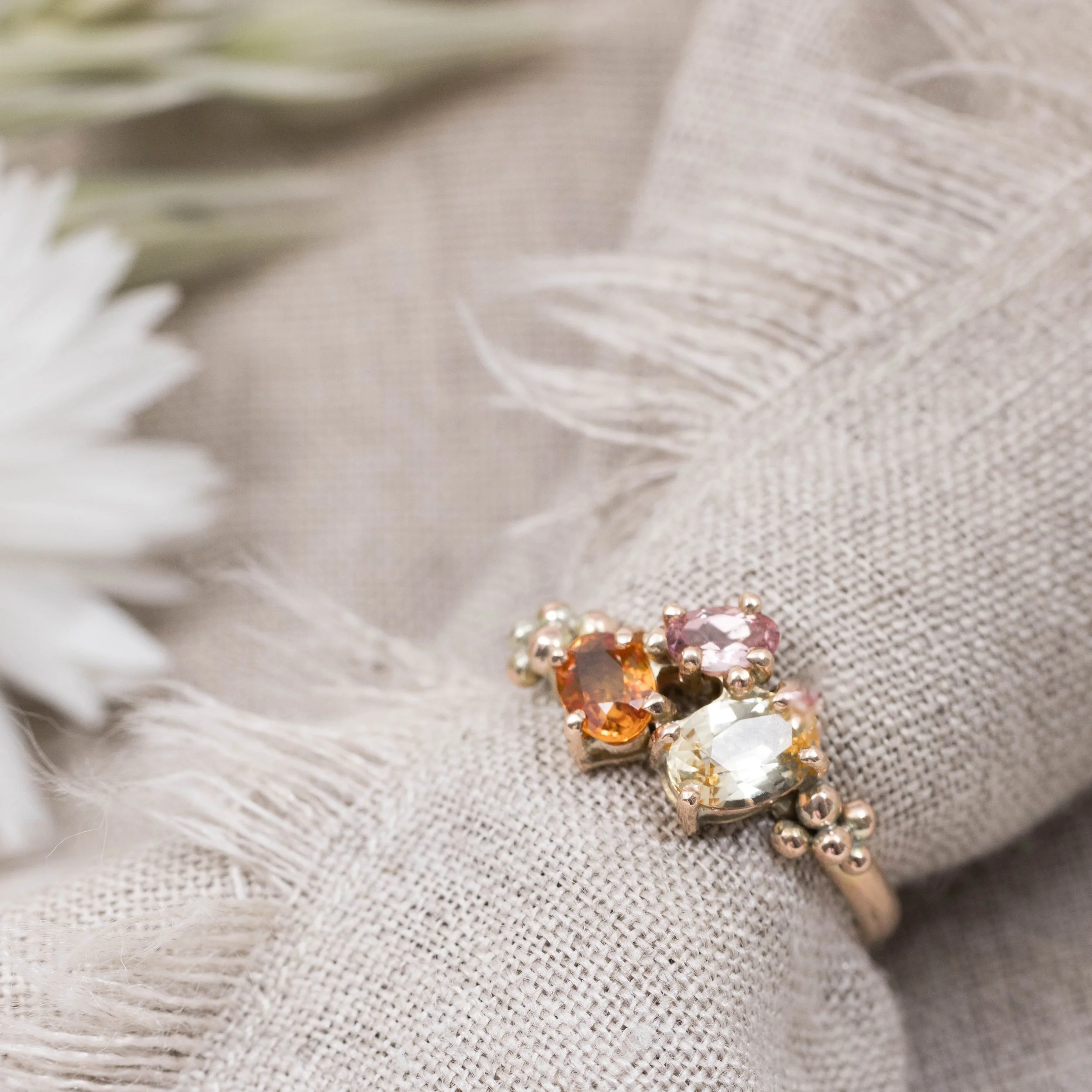 Rose gold ring with an oval orange sapphire centre surrounded by a cluster of round pink and yellow sapphires.