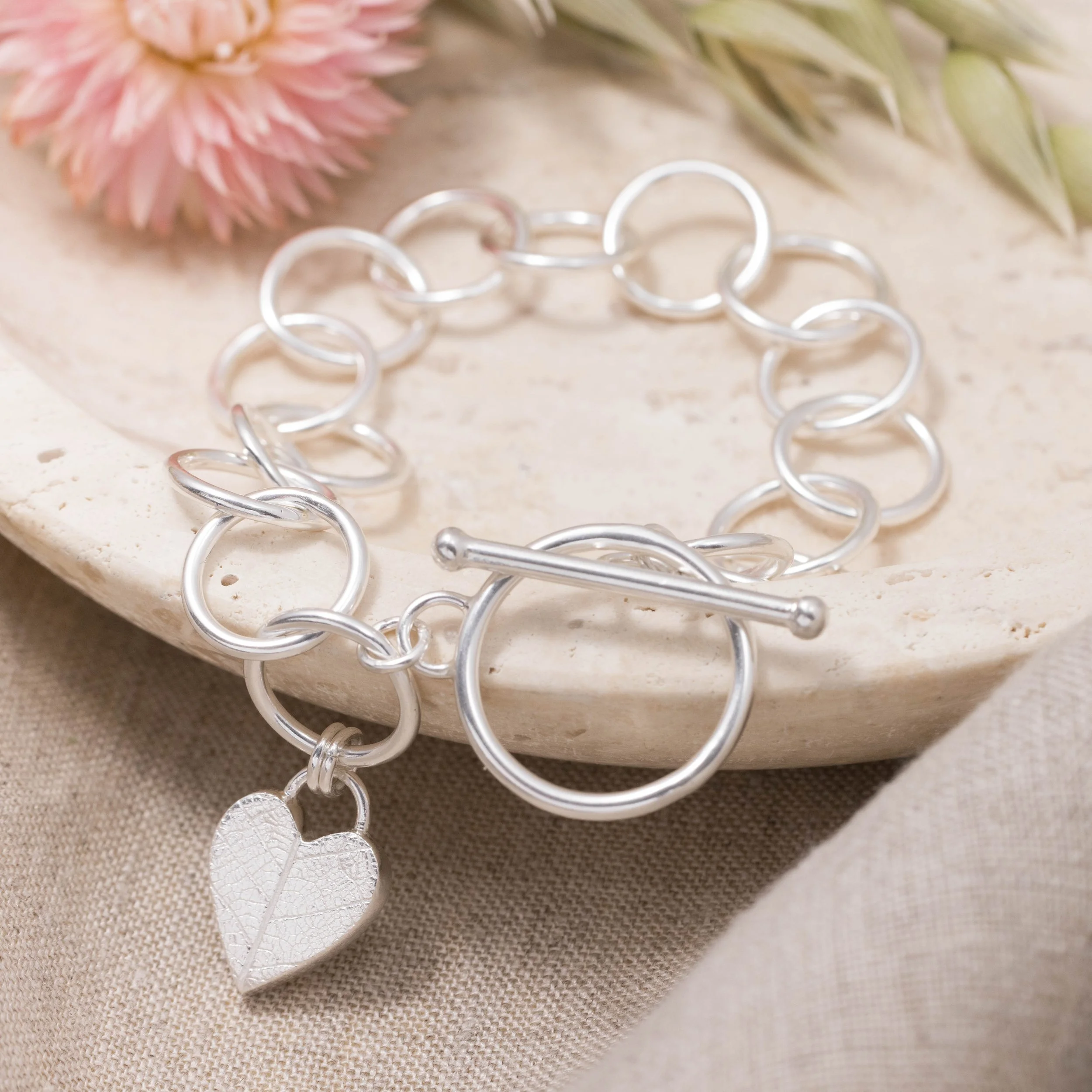 Sterling silver bracelet with a textured heart charm featuring a delicate leaf pattern, finished with a toggle clasp.