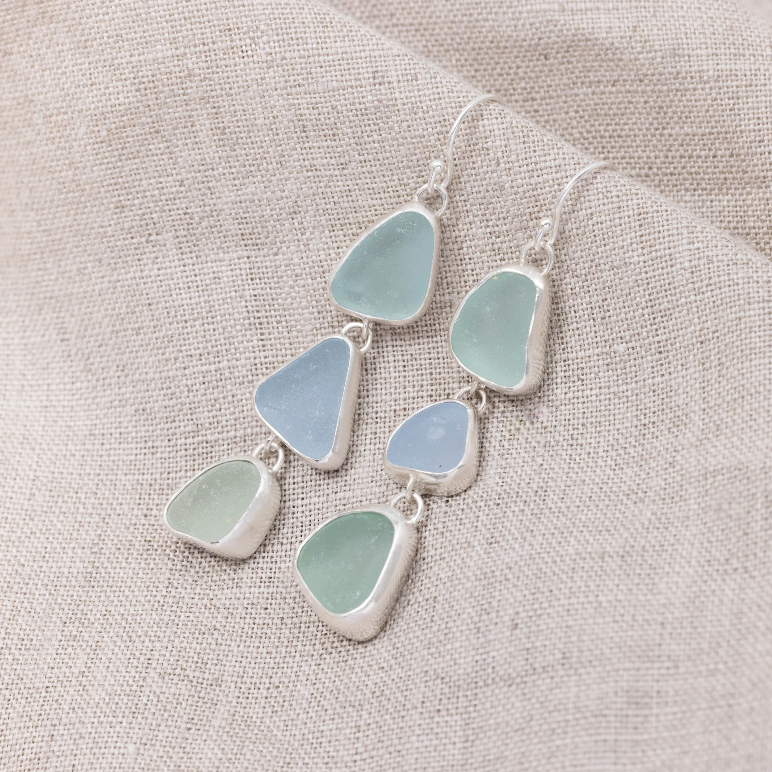 Sterling silver drop earrings with cascading multi-coloured sea glass pieces in green and blue tones on delicate ear wires. Coastal inspired jewellery design.