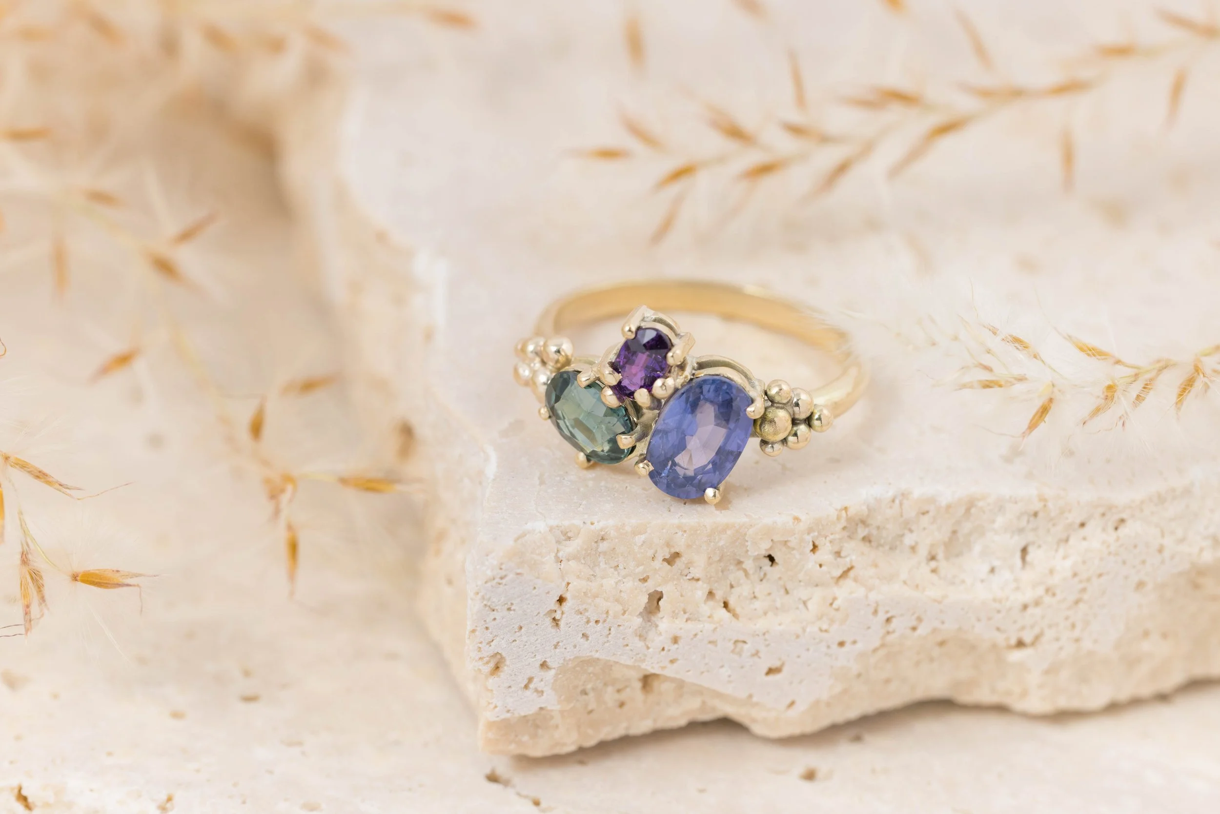 Yellow gold ring with a cluster of sparkling saaphires in teal, deep blue, and purple. Inspired by the colours of the aurora borealis.