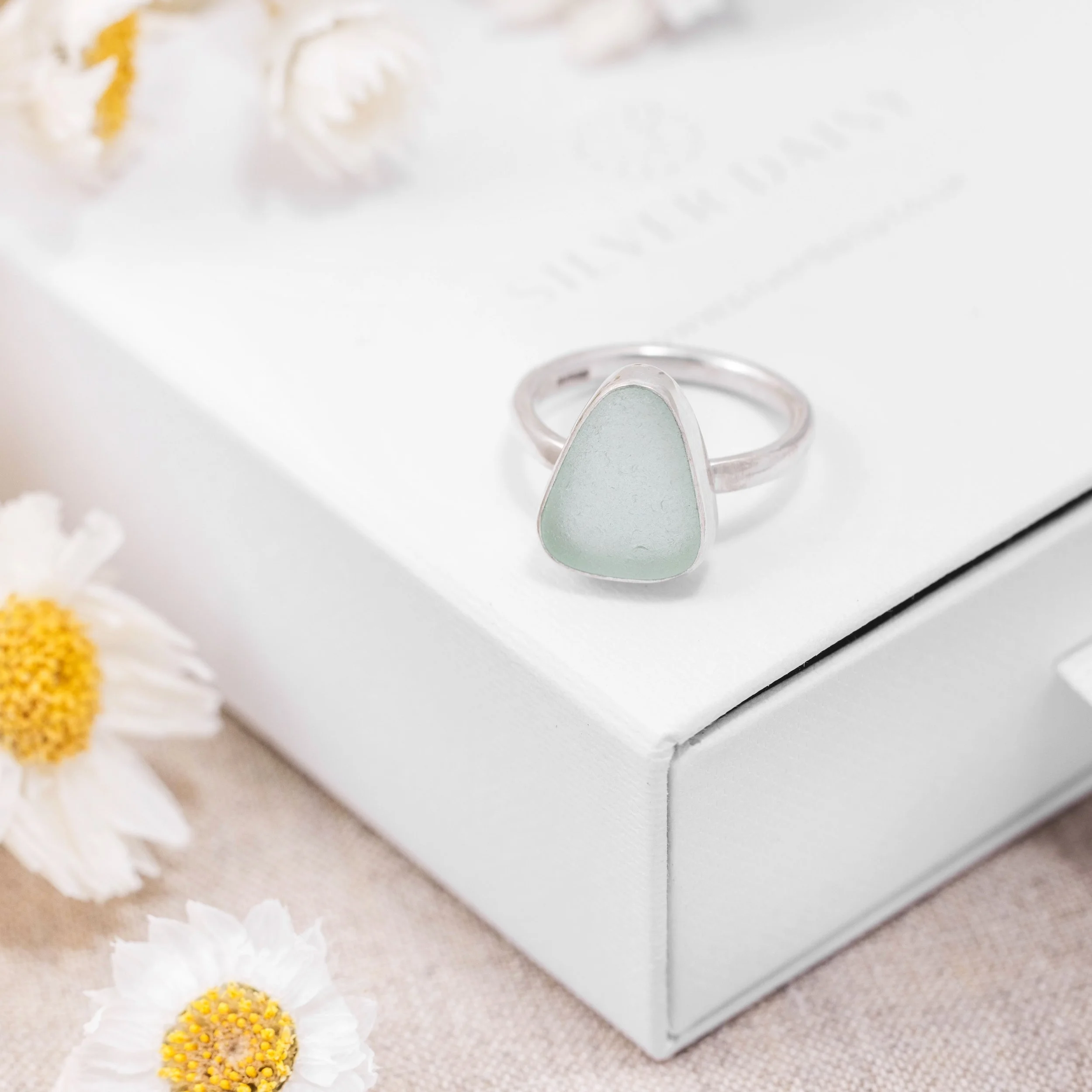 Sterling silver ring with a smooth aquamarine sea glass gemstone in a polished bezel setting on a slim oval band. Coastal beach inspired jewellery.