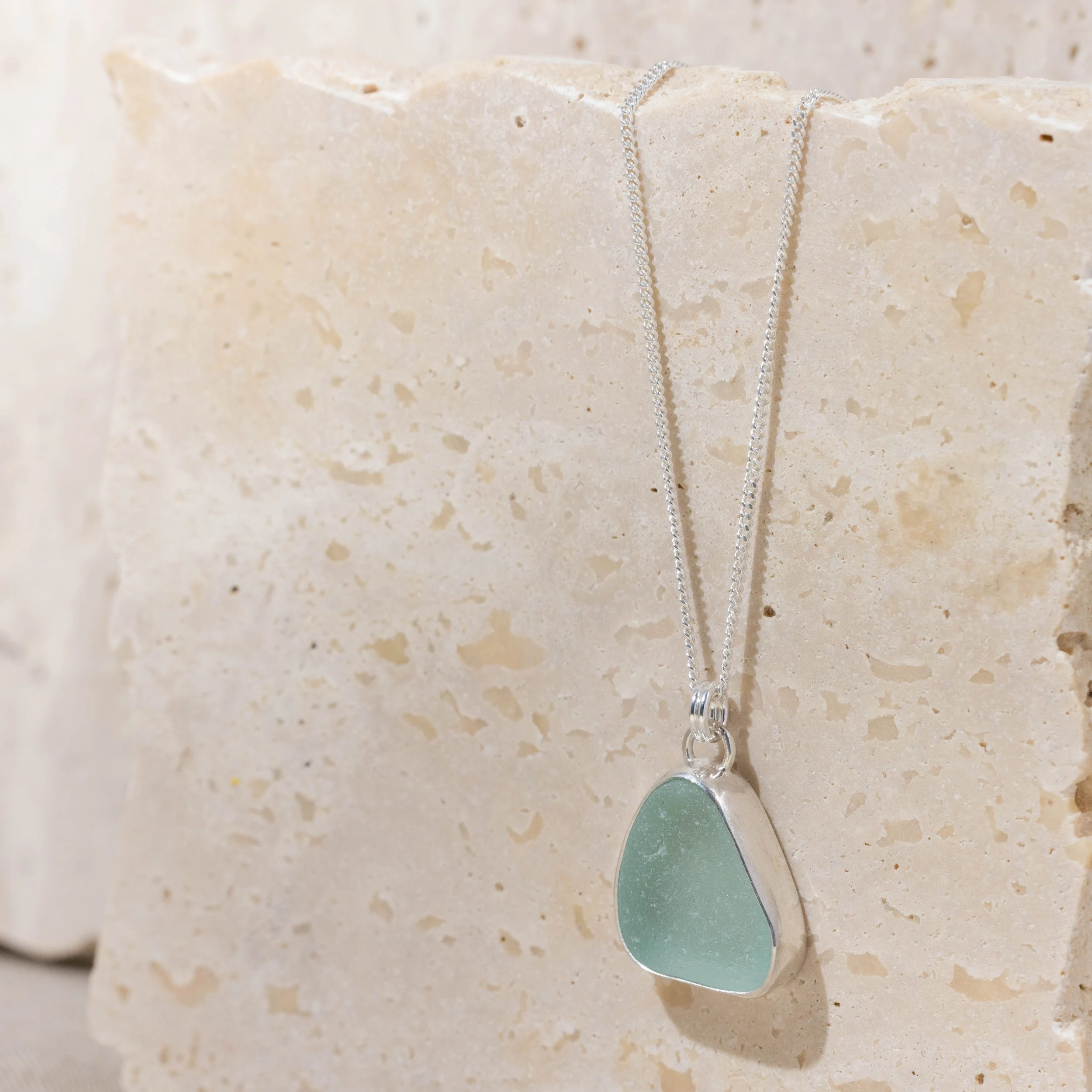 Aqua sea glass pebble set in polished silver on a delicate chain, coastal-inspired handmade necklace.