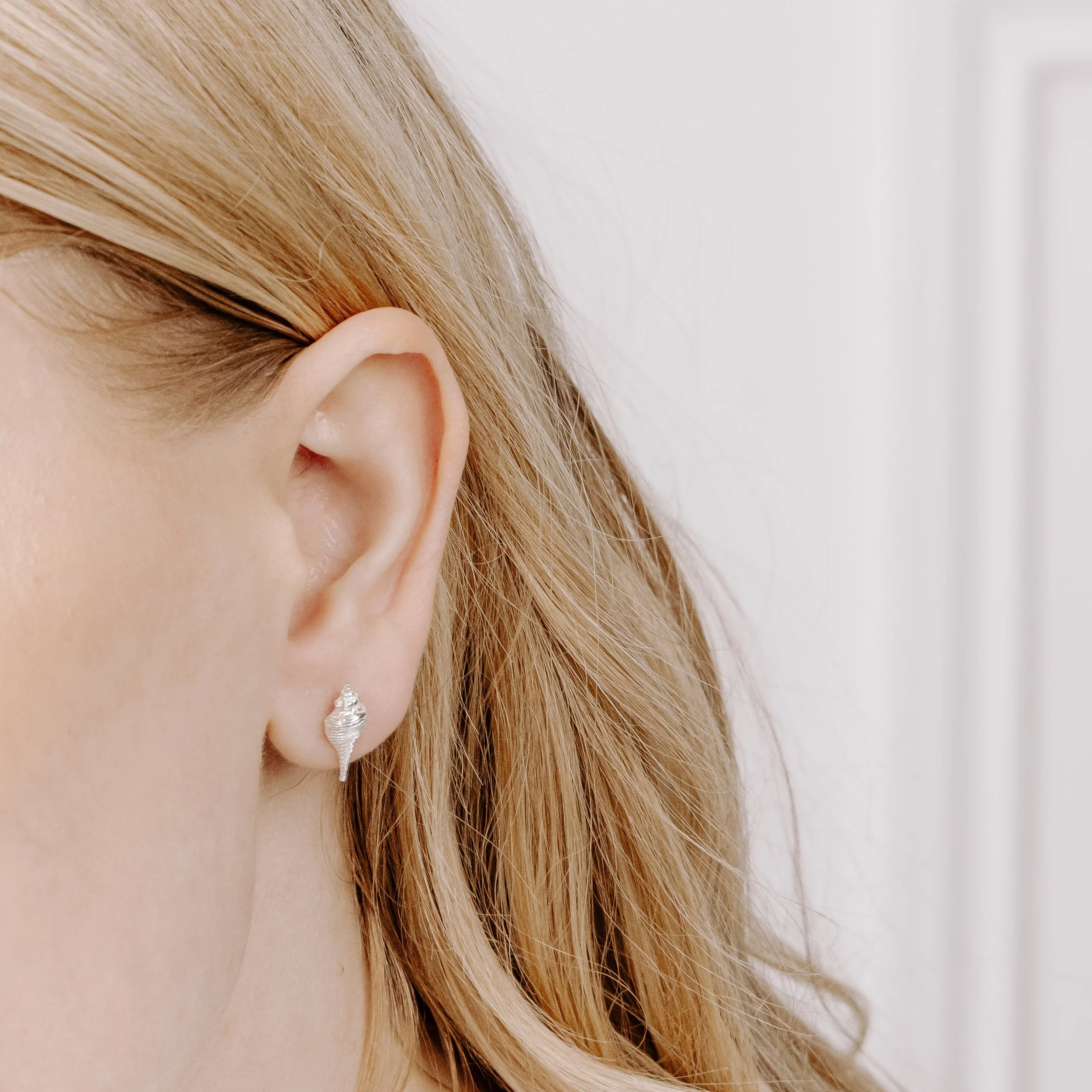 Dainty sterling silver conch shell stud earrings with polished finish, inspired by coastal seashell designs.