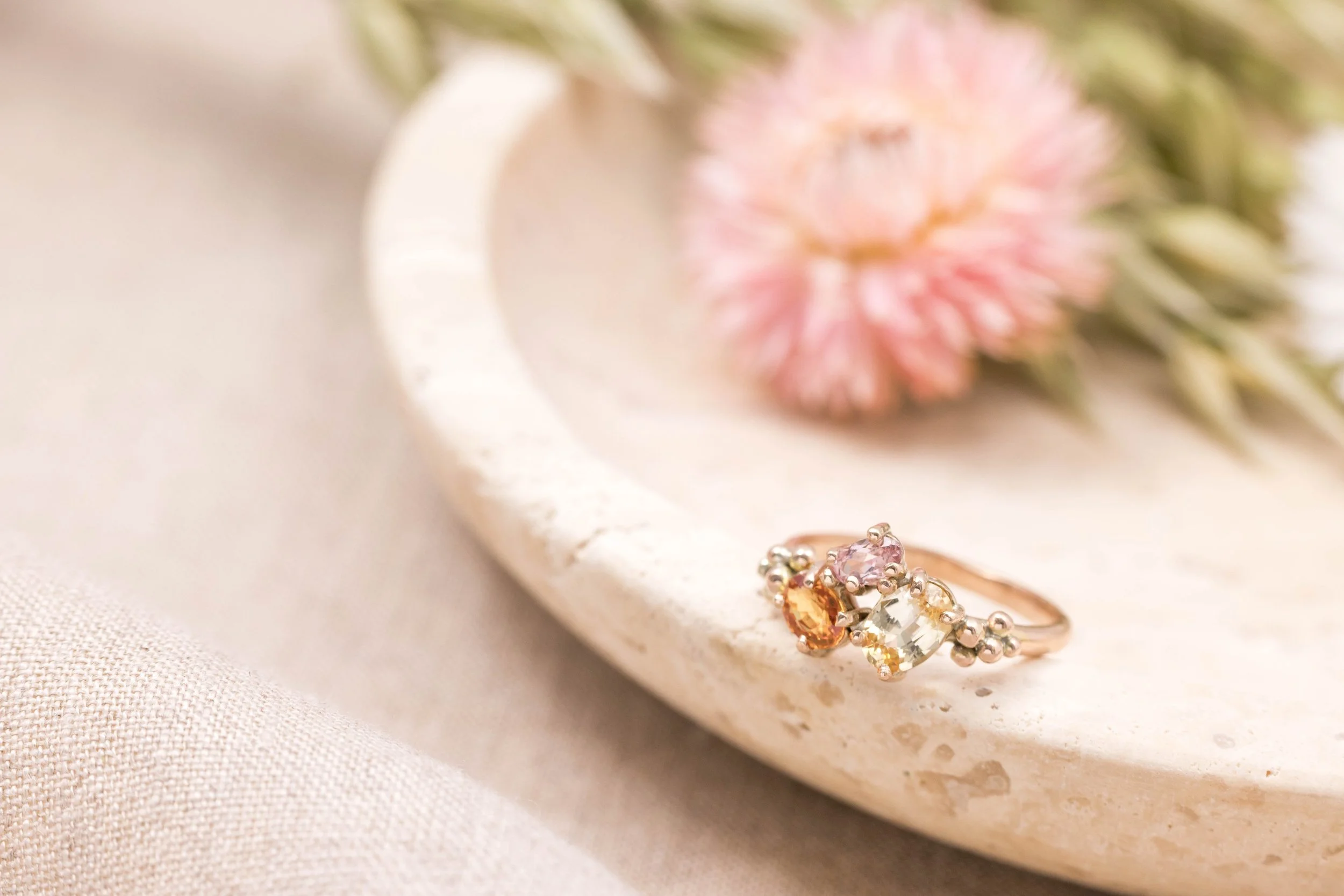 Rose gold ring with an oval orange sapphire centre surrounded by a cluster of round pink and yellow sapphires.