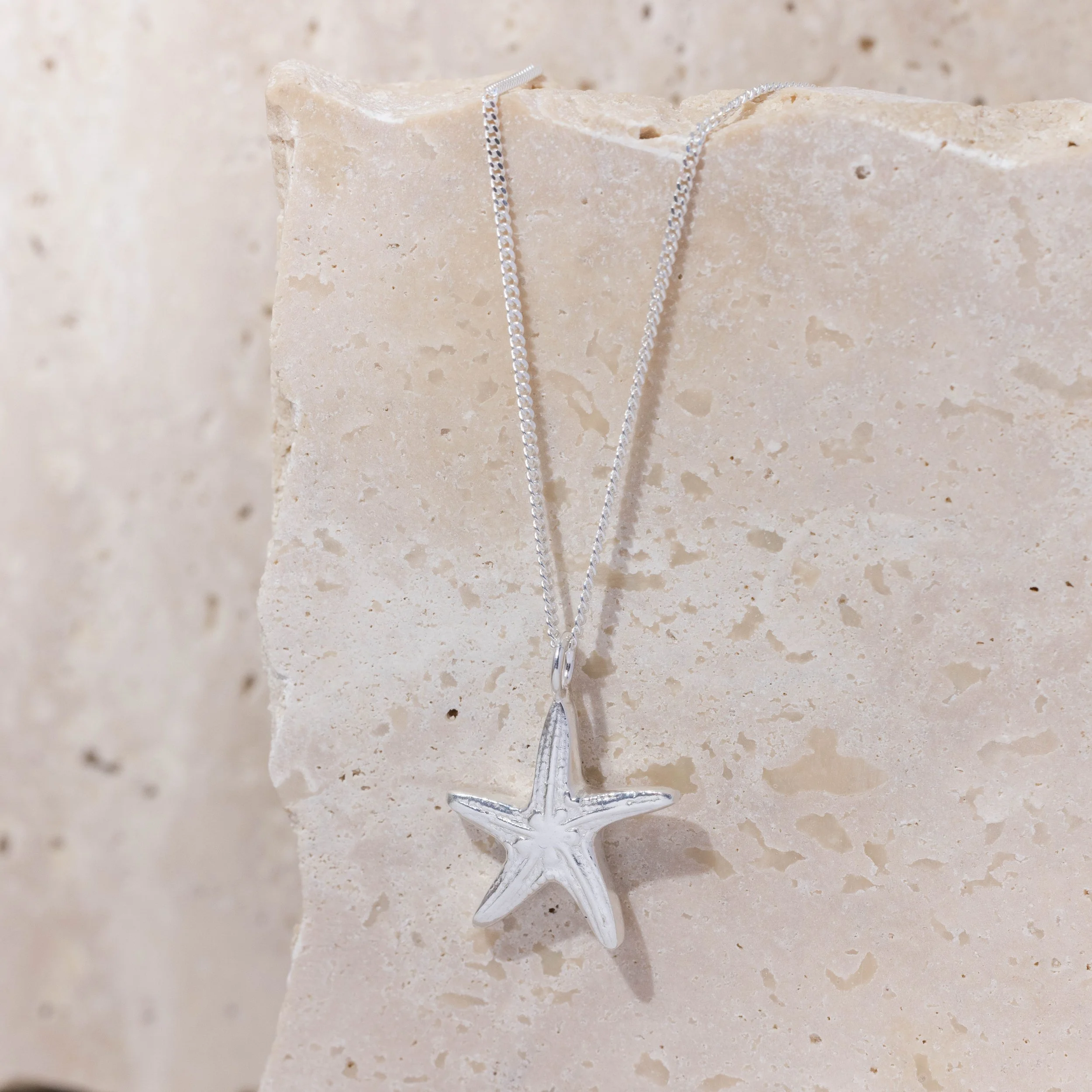 Sterling silver starfish pendant necklace with delicate chain, featuring textured detailing inspired by coastal marine life.