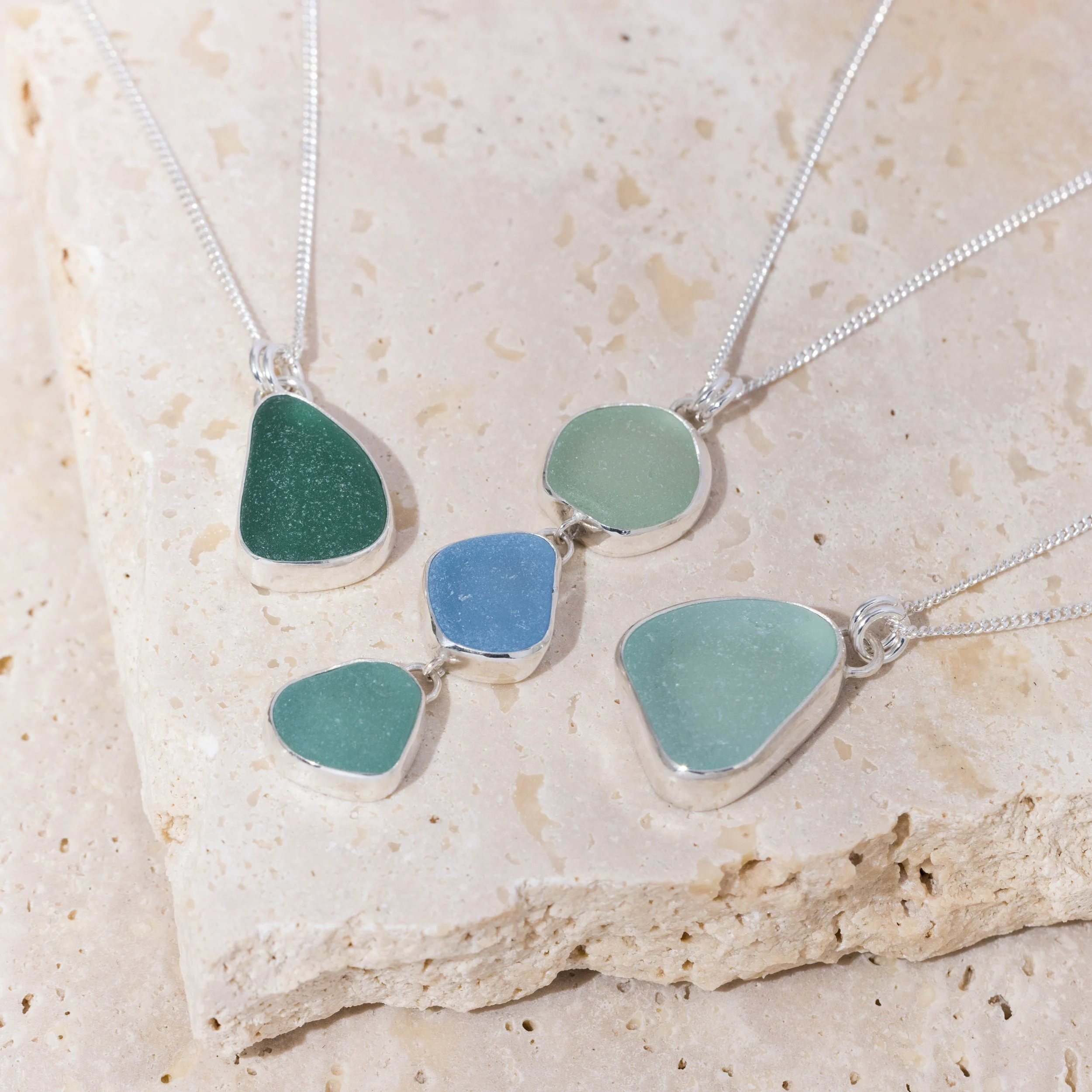 Sterling silver pendant necklace with cascading multi-coloured sea glass drops in green and blue tones, inspired by coastal style.