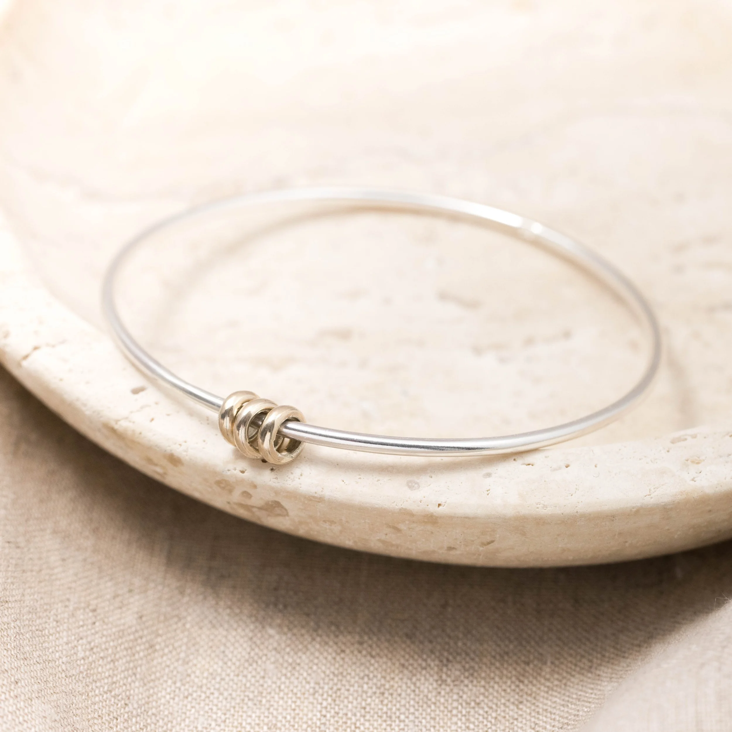 Sterling silver bangle with polished 9ct gold satellite rings which move freely around the band. An elegant fidget bracelet.