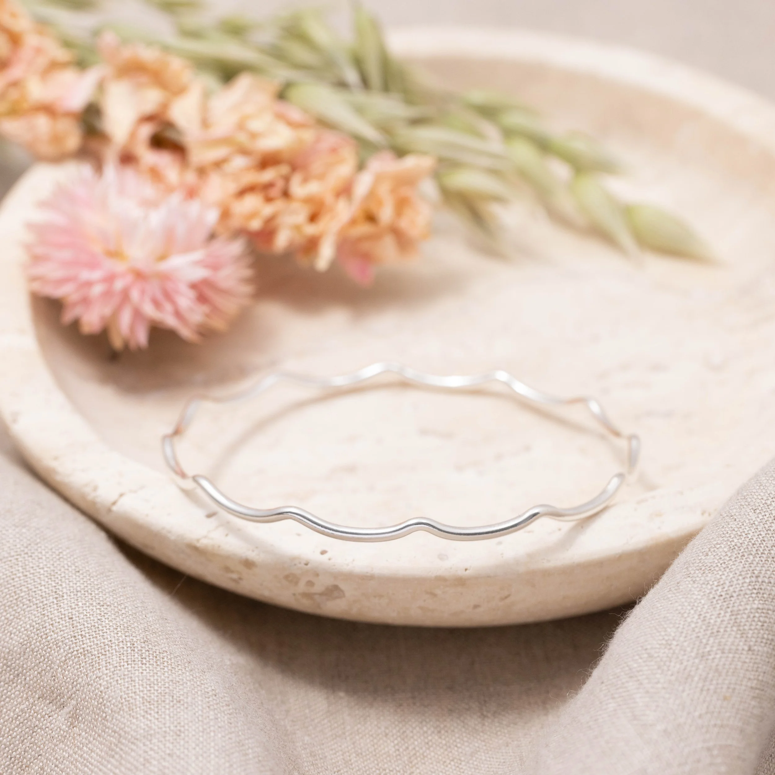 Slim sterling silver stacking bangle with a polished wave design, perfect for layering in a modern minimalist style or simply worn alone.