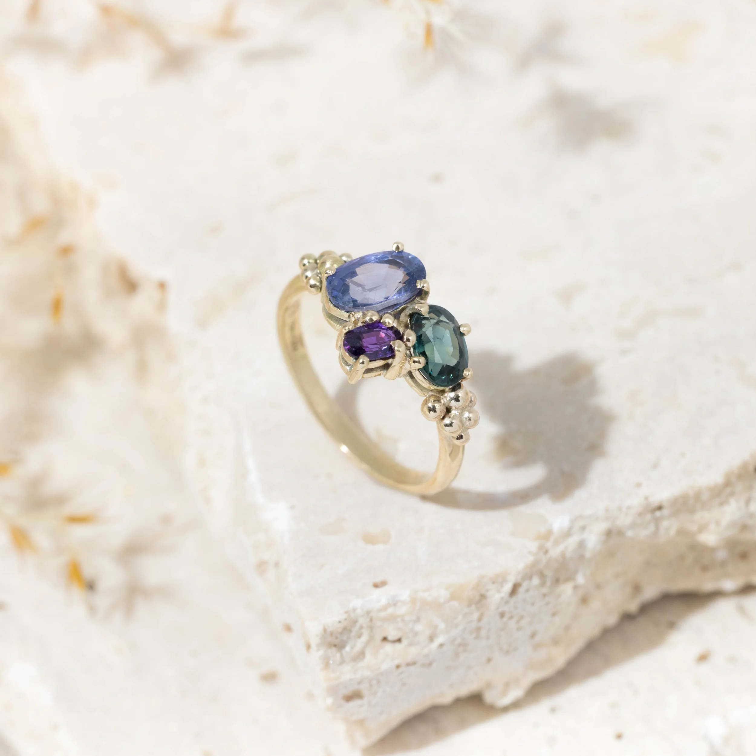 Yellow gold ring with a cluster of sparkling saaphires in teal, deep blue, and purple. Inspired by the colours of the aurora borealis.