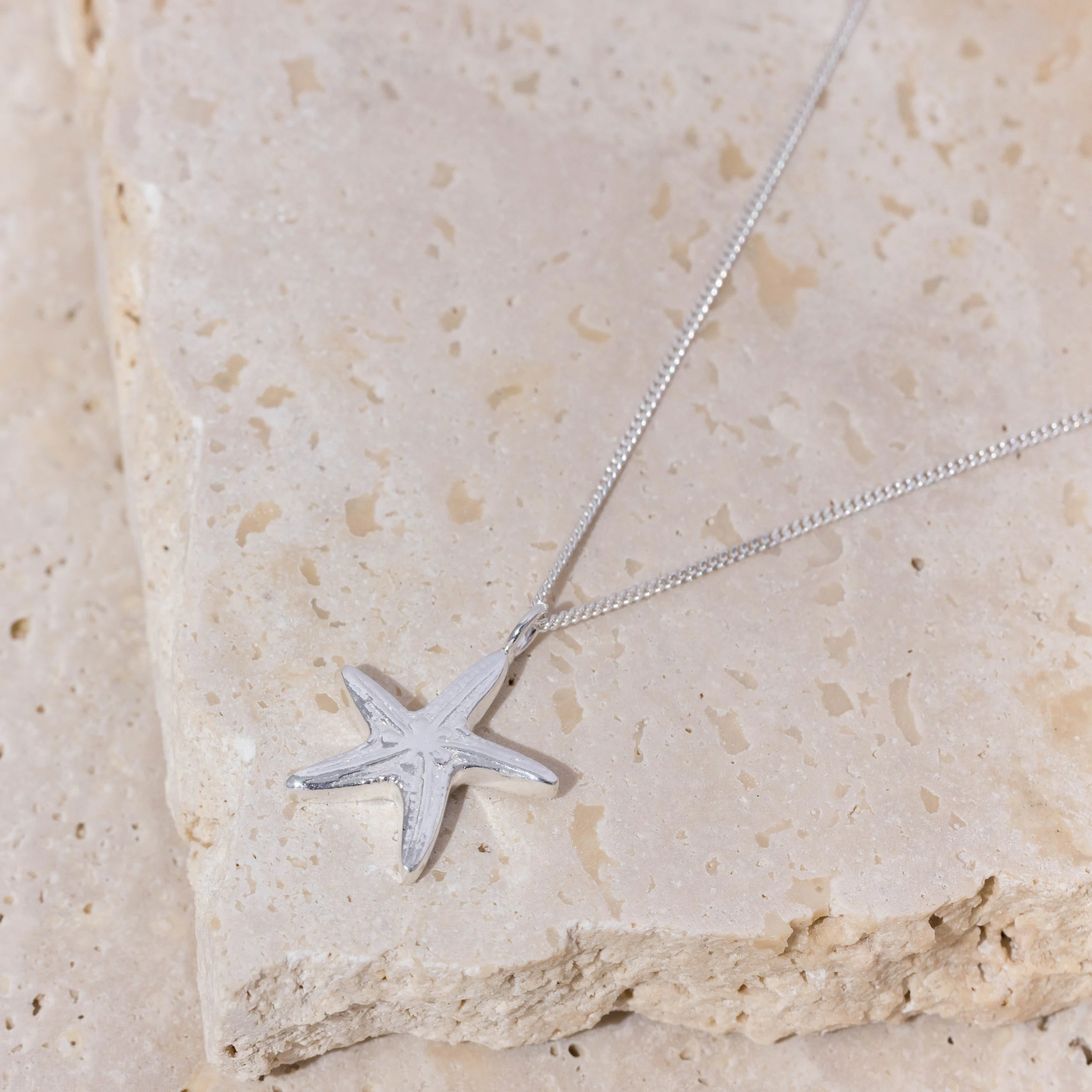 Sterling silver starfish pendant necklace with delicate chain, featuring textured detailing inspired by coastal marine life.