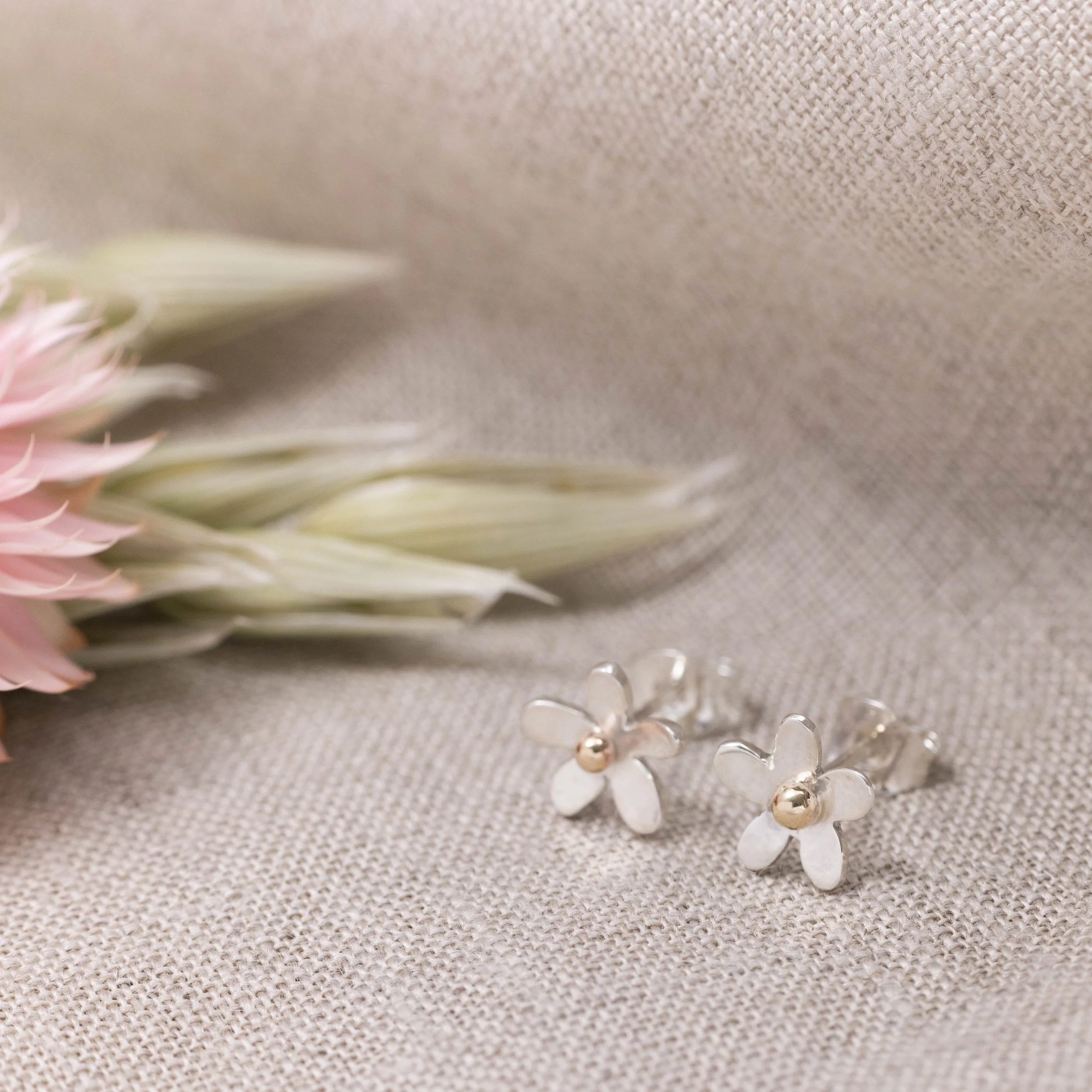 Small sterling silver daisy stud earrings with polished petals and 9ct gold stamen centres.