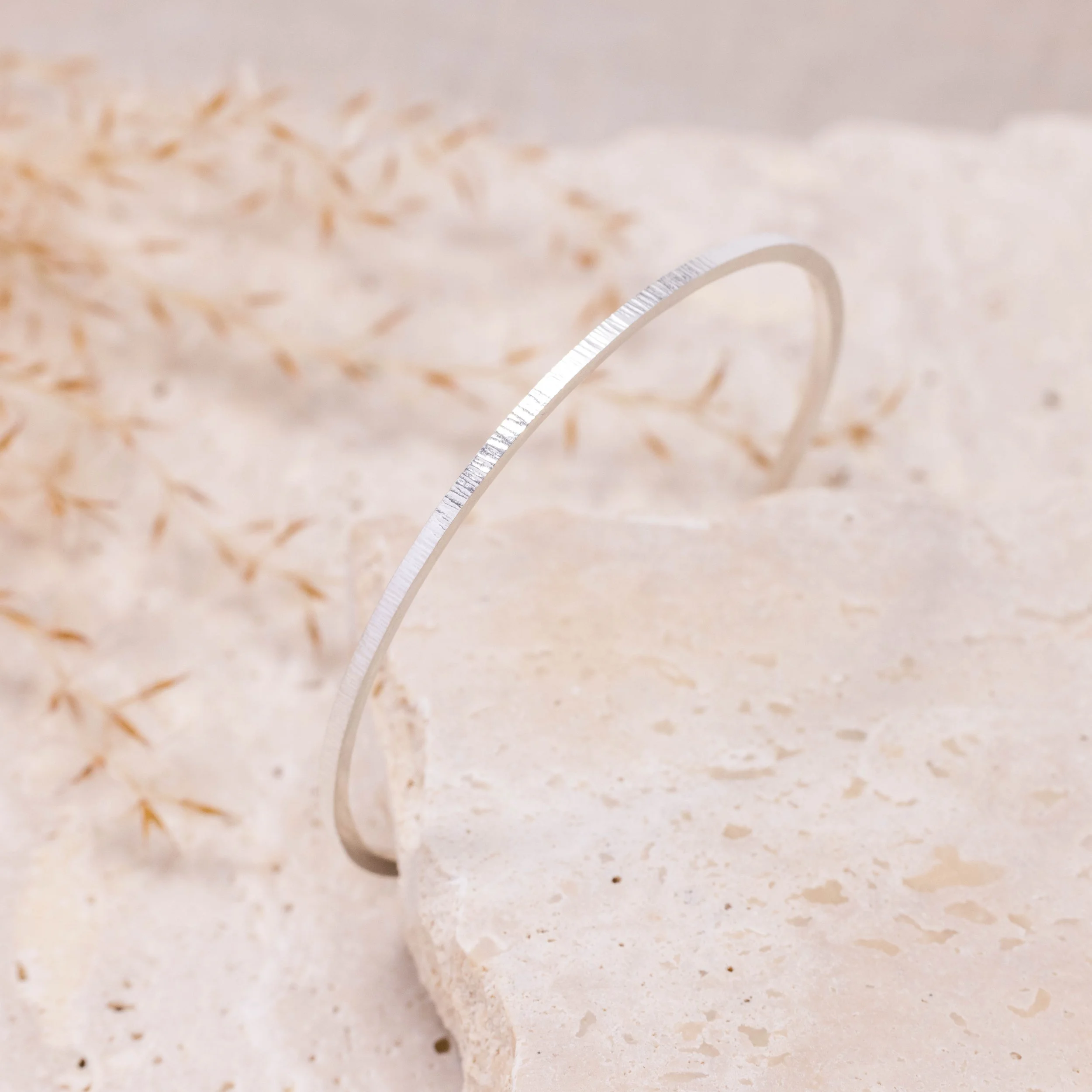 Slim sterling silver stacking bangle with a hammered line texture, polished finish, and minimalist contemporary design.