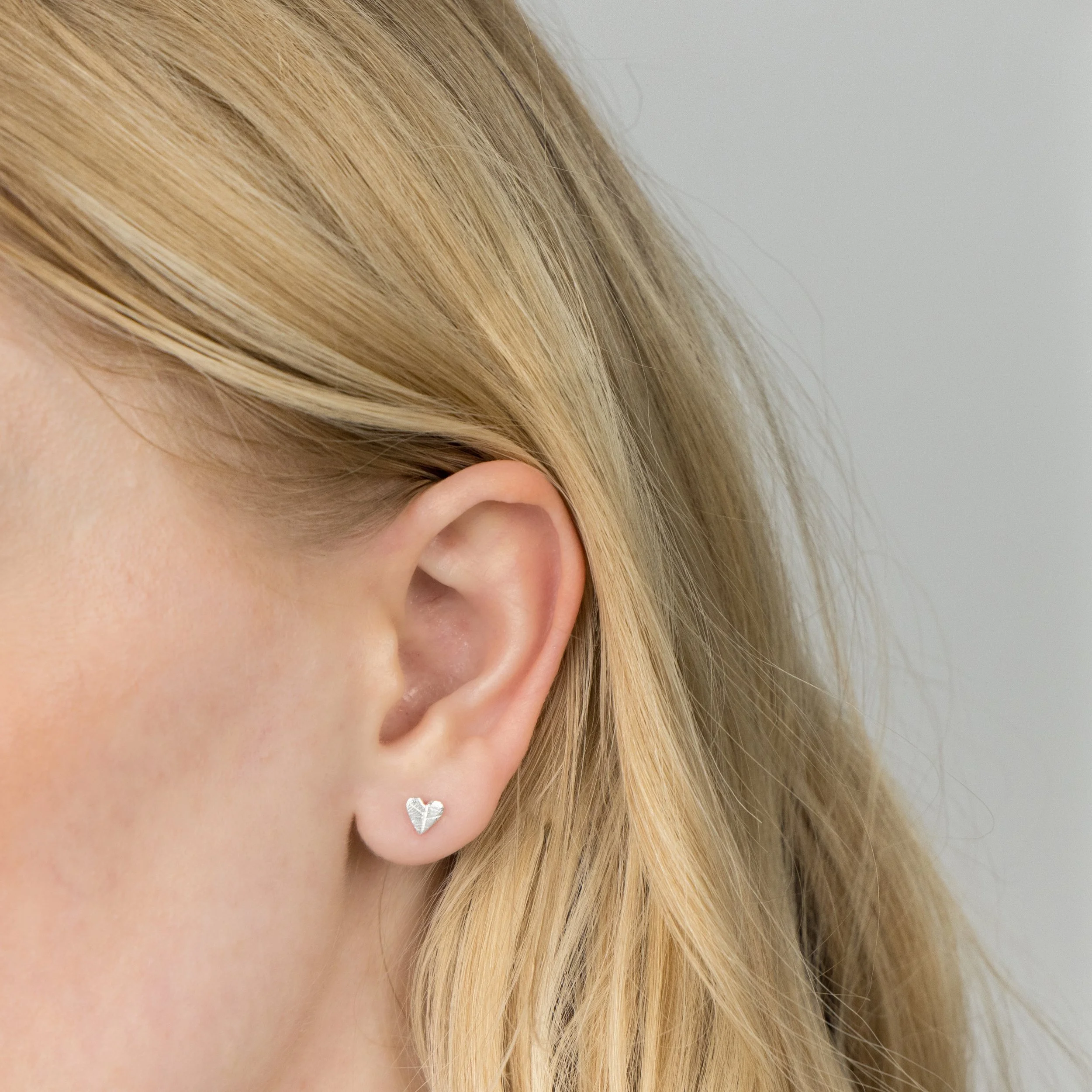 Mini sterling silver heart stud earrings with delicate leaf vein texture, polished finish, and butterfly backs.