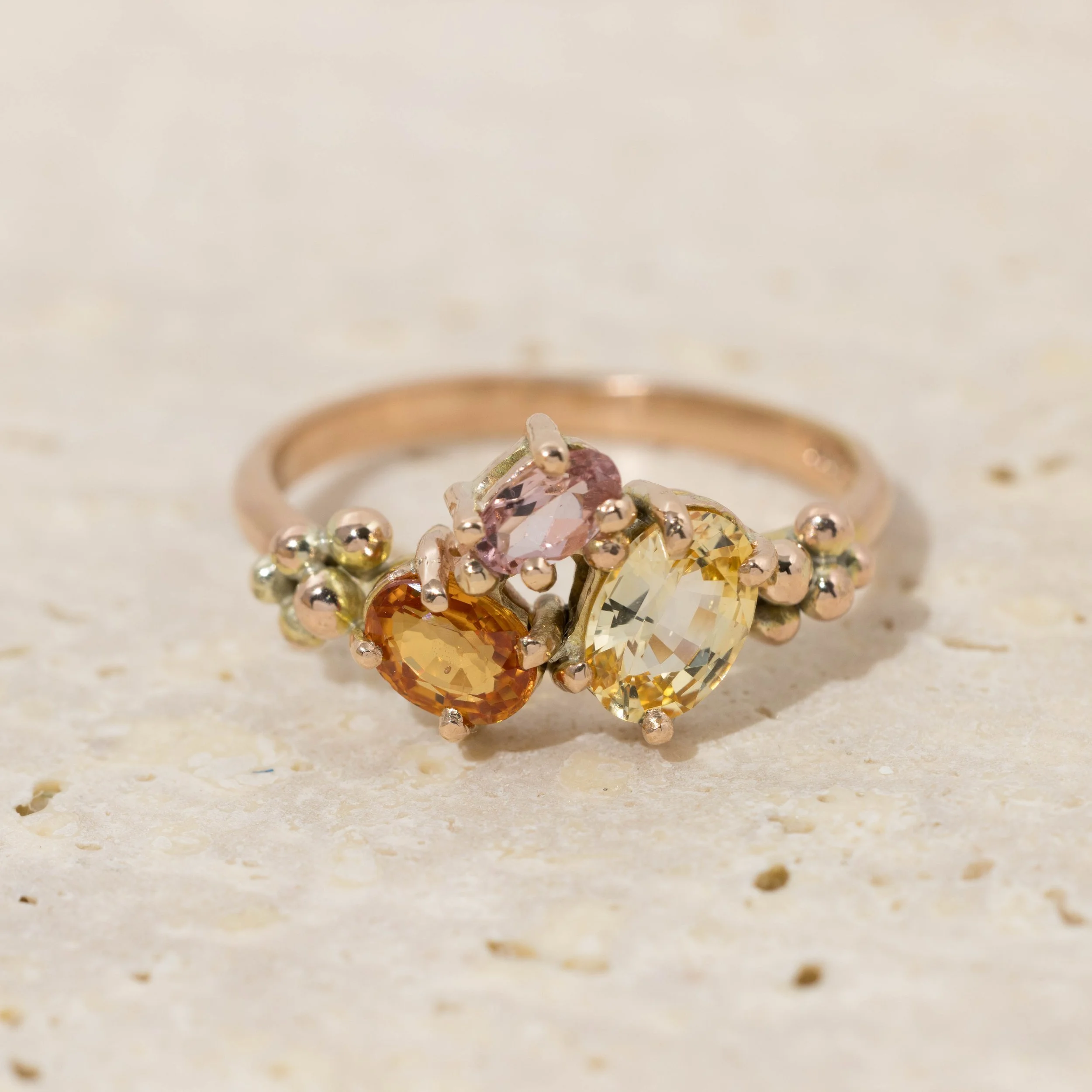 Rose gold ring with an oval orange sapphire centre surrounded by a cluster of round pink and yellow sapphires.