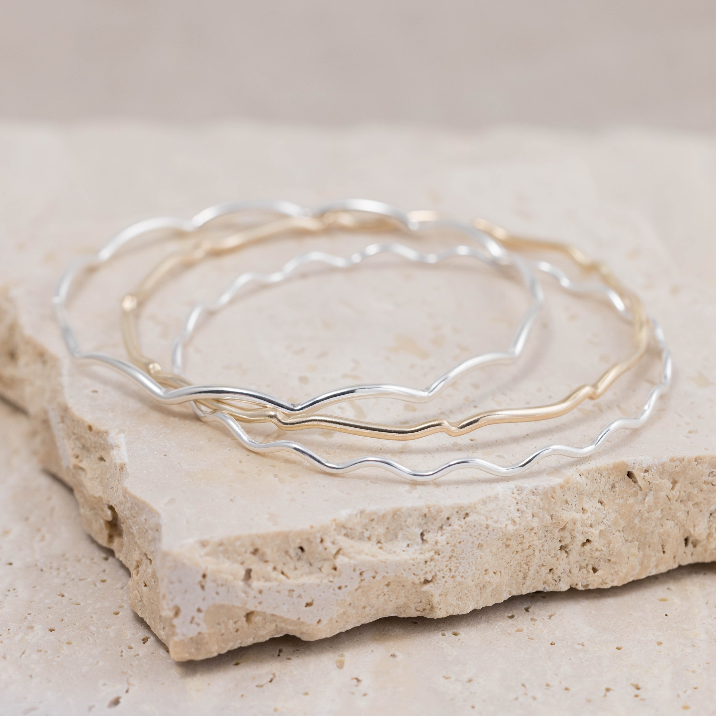 Slim sterling silver stacking bangle with a polished wave design, perfect for layering in a modern minimalist style or simply worn alone.
